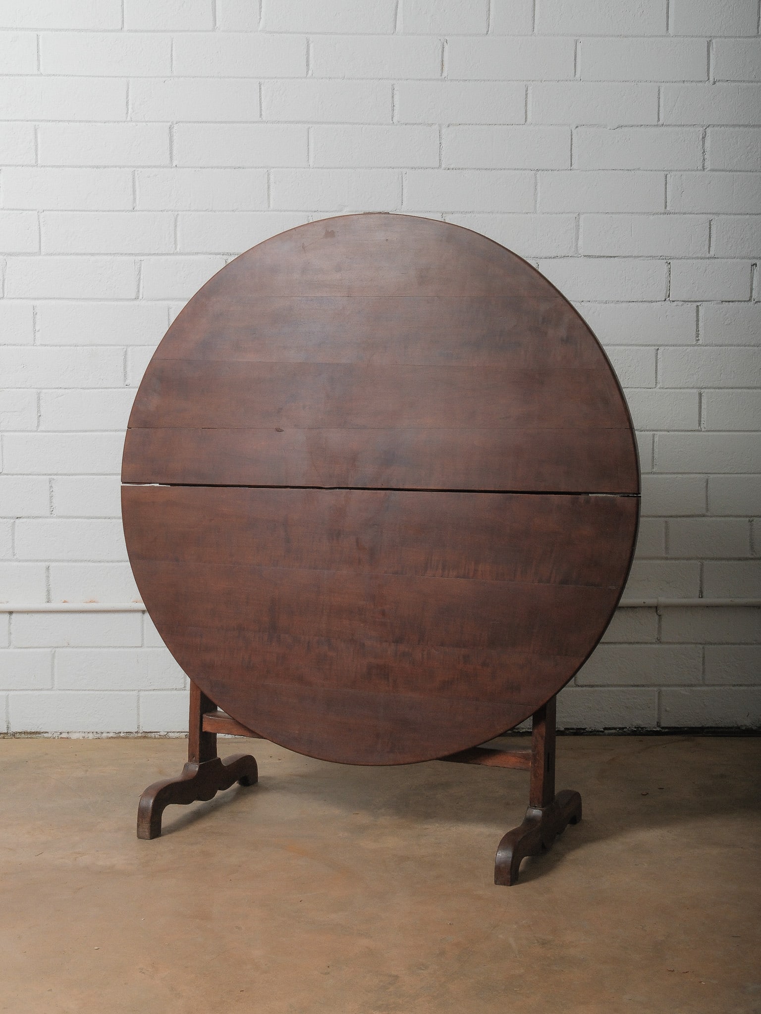 French Flip Top Wine Table: Beautiful large French tilt-top table featuring a round plank-constructed top supported by a trestle base with shaped feet. The tabletop pivots vertically on original iron brackets, allowing the piece