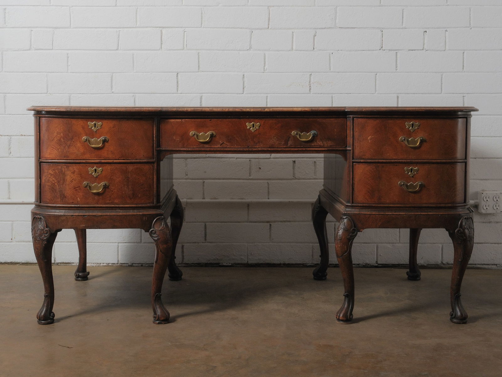 Antique Carved Walnut Writing Desk: Early 20th-century walnut writing desk with a serpentine front, cabriole legs, and carved shell motifs. Features five deep drawers with brass bail pulls and a wide center kneehole opening. Beautiful w
