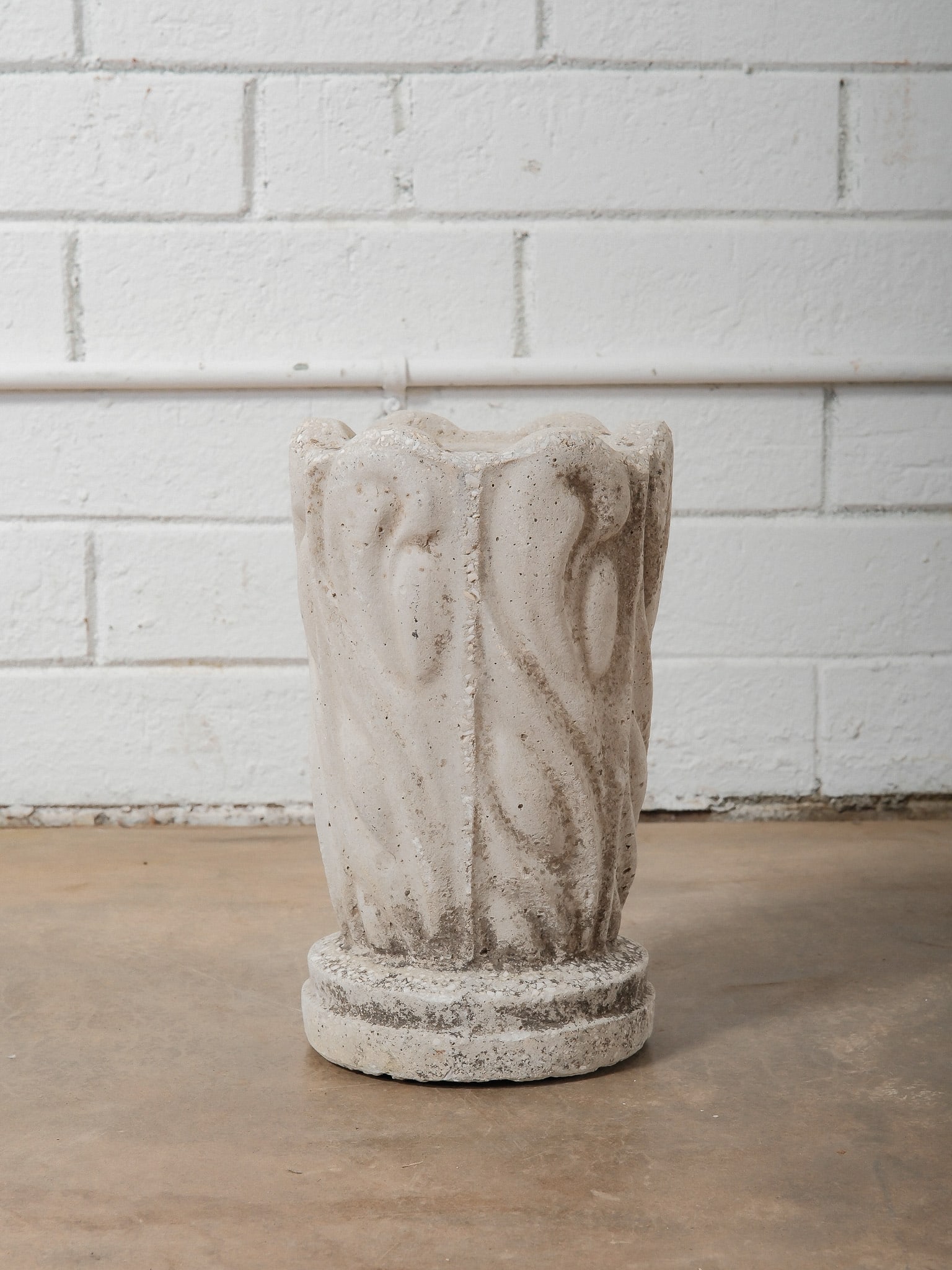 Small Cast Concrete Planter: This small cast concrete planter features softly carved vertical relief detailing and a naturally weathered surface. Classical in form, it has a gently flared rim and a raised circular base, giving