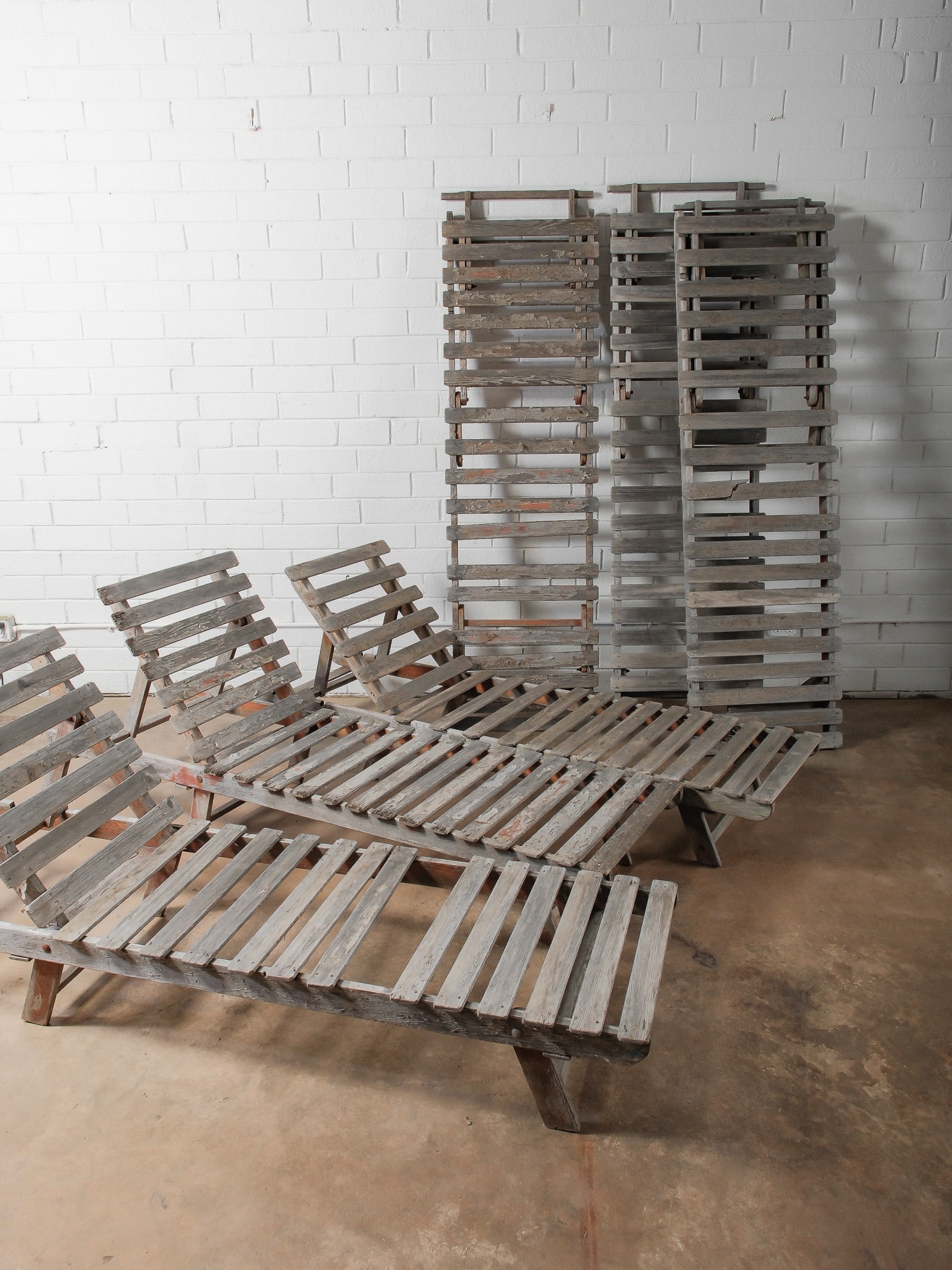 Set of 6 Rustic Sun Loungers: Group of folding wooden slat lounge chairs with adjustable backs. Distressed painted finish and visible age-related wear. Suitable for porch or garden styling.