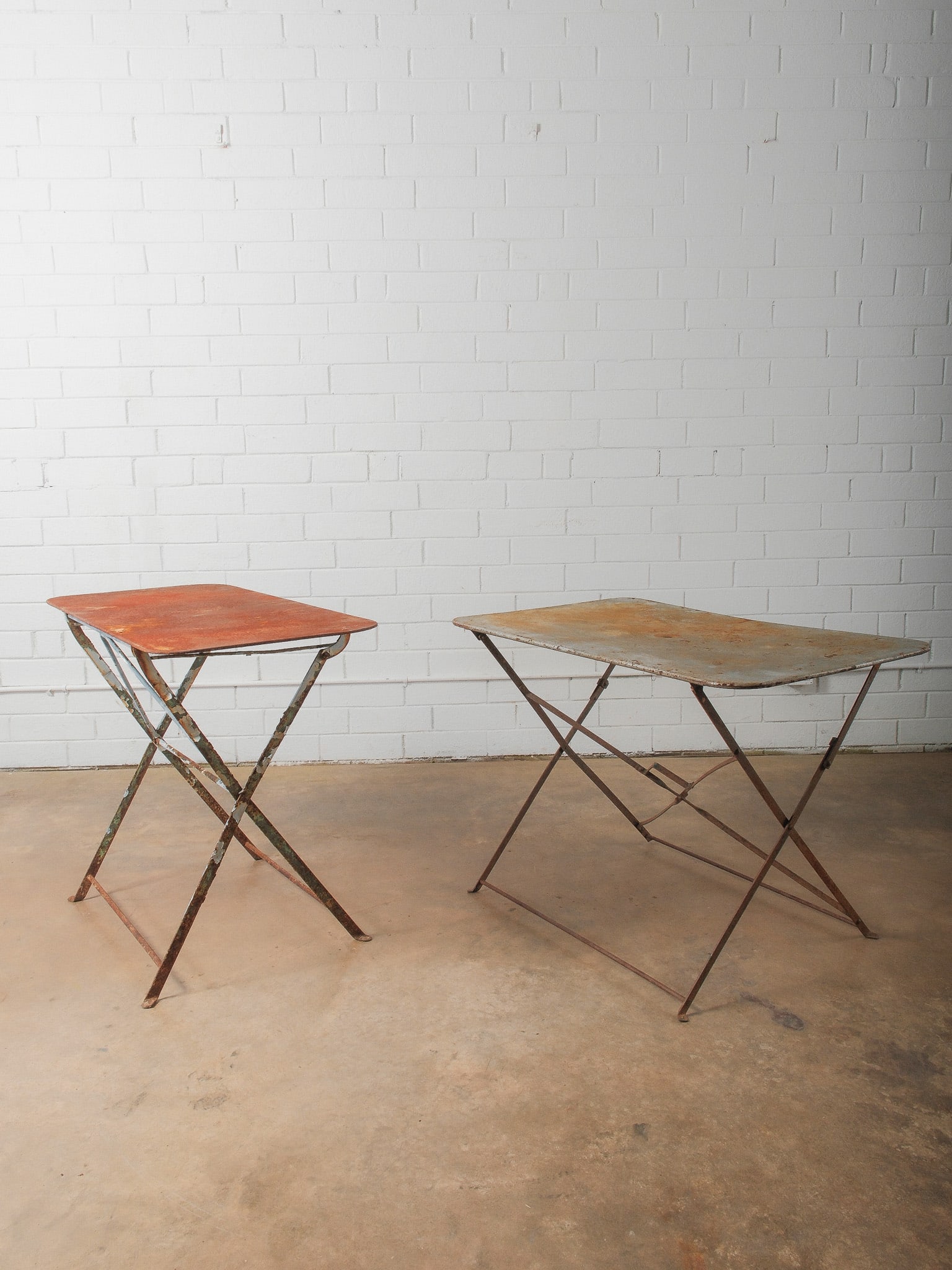 Pair of Vintage Folding Metal Tables: Pair of metal folding tables with rectangular tops and crossed leg supports. Surfaces show layered paint and natural patina from age and use. Functional and versatile suitable for garden, patio, or in