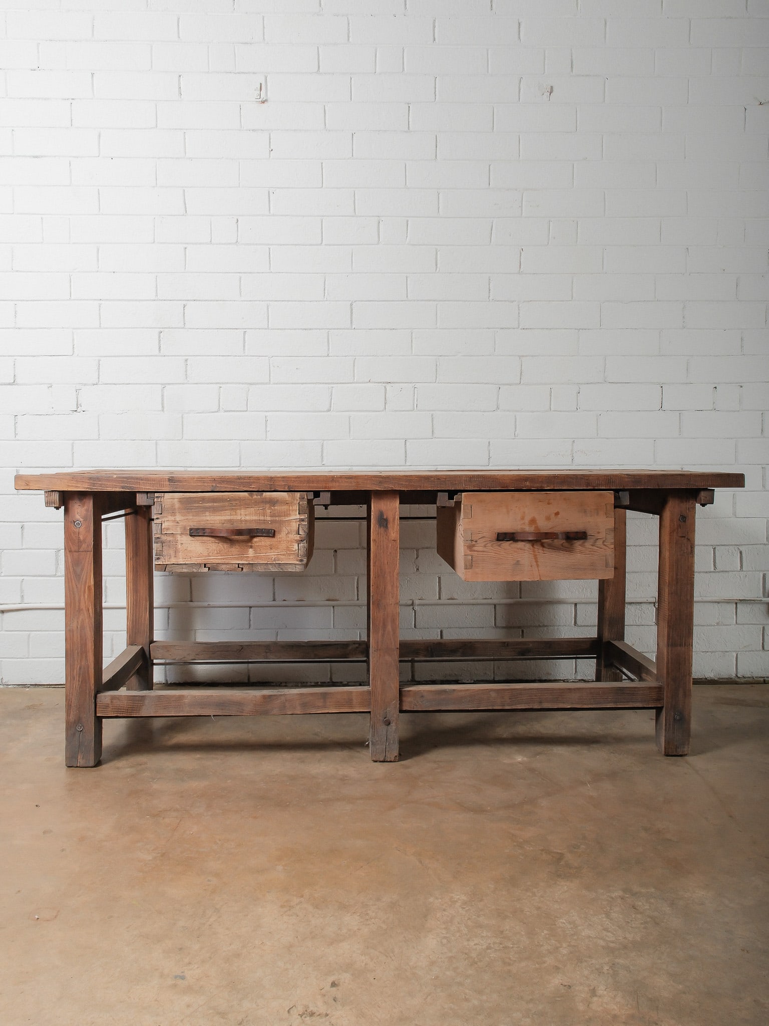 Rustic Work Table: A substantial rustic work table crafted from solid wood, showcasing a thick plank top with visible grain and natural wear. The table features two built-in drawers with simple iron pulls and sturdy tre