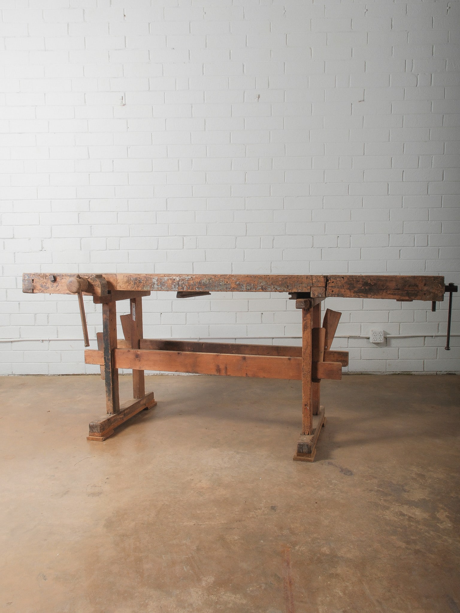 Carpenters Workbench with Vise: Solid wood workbench featuring built-in vise and thick plank top. Heavy trestle-style base construction. Excellent as-is industrial statement piece or functional shop bench.
