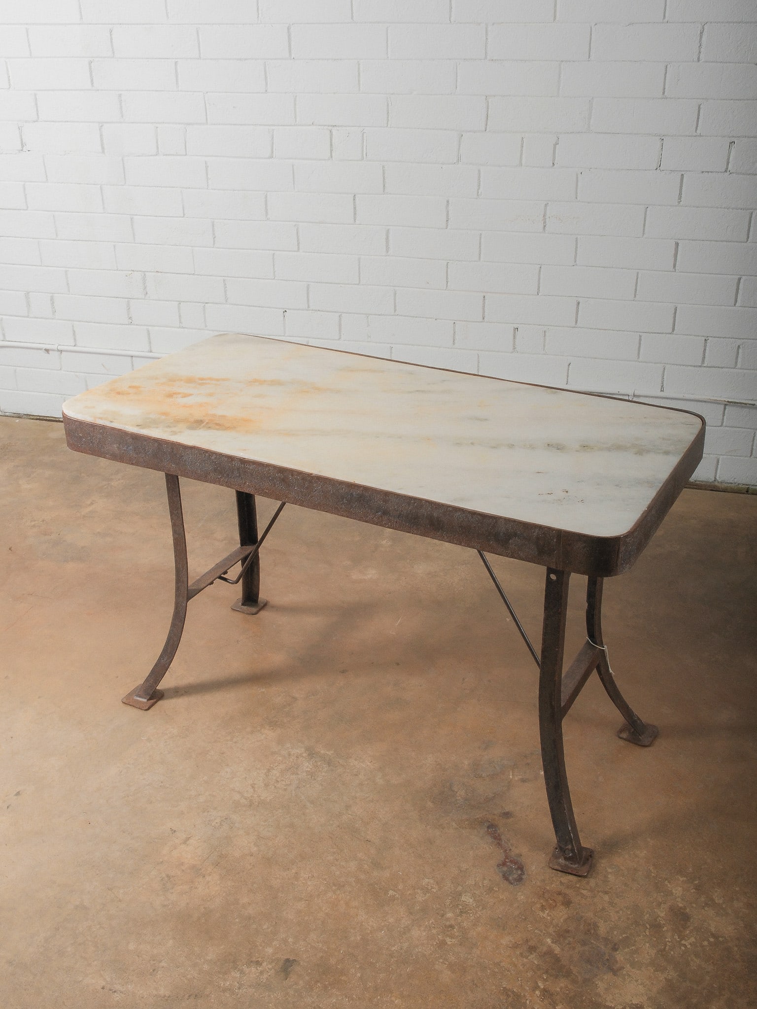 Industrial Marble-Top Work Table: Rectangular marble slab top set within iron frame base. Curved iron legs with cross supports. Strong industrial aesthetic ideal as kitchen island, prep table, or statement console.
