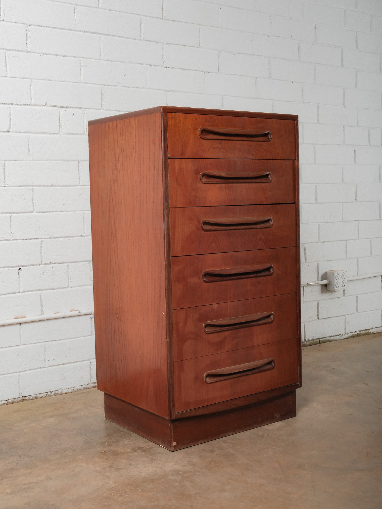 G PLAN Six-Drawer Chest: This mid-century modern chest features six stacked drawers with sculpted integrated pulls. Finished in a warm wood tone, the piece rests on a recessed base and showcases clean lines and subtle