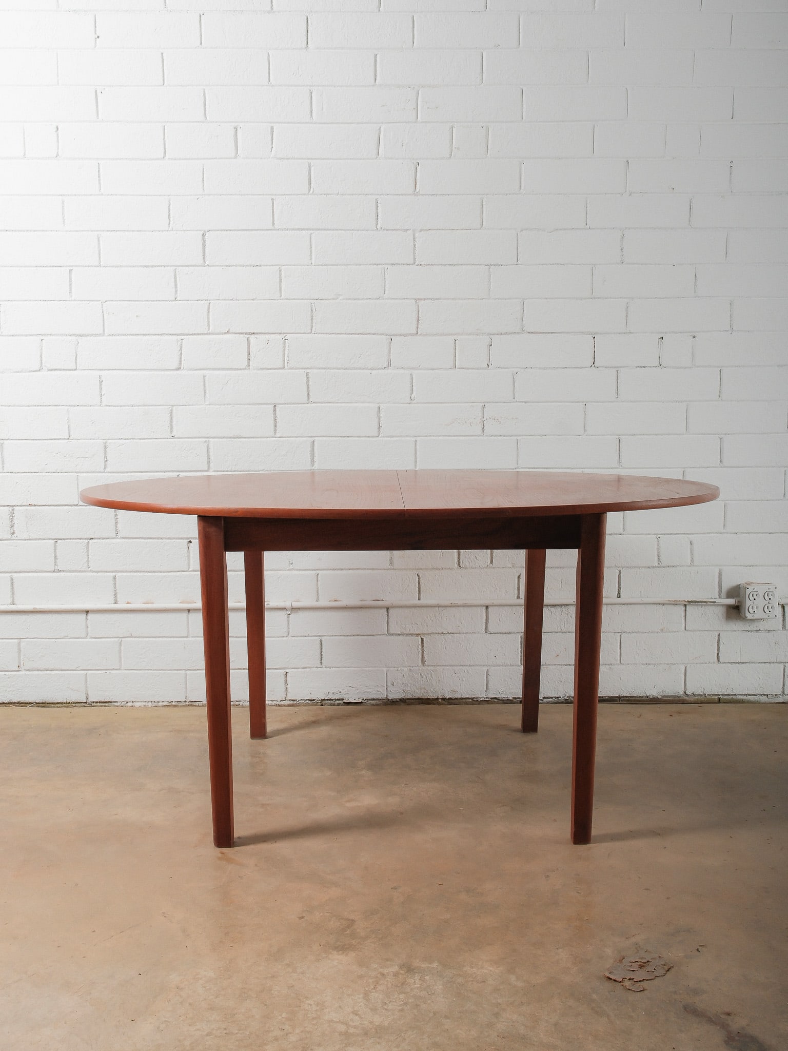 MCM Oval Dining Table: This mid-century modern dining table features an oval top with softly rounded edges supported by four straight legs. Finished in a warm wood tone, the table clean lines and balanced proportions