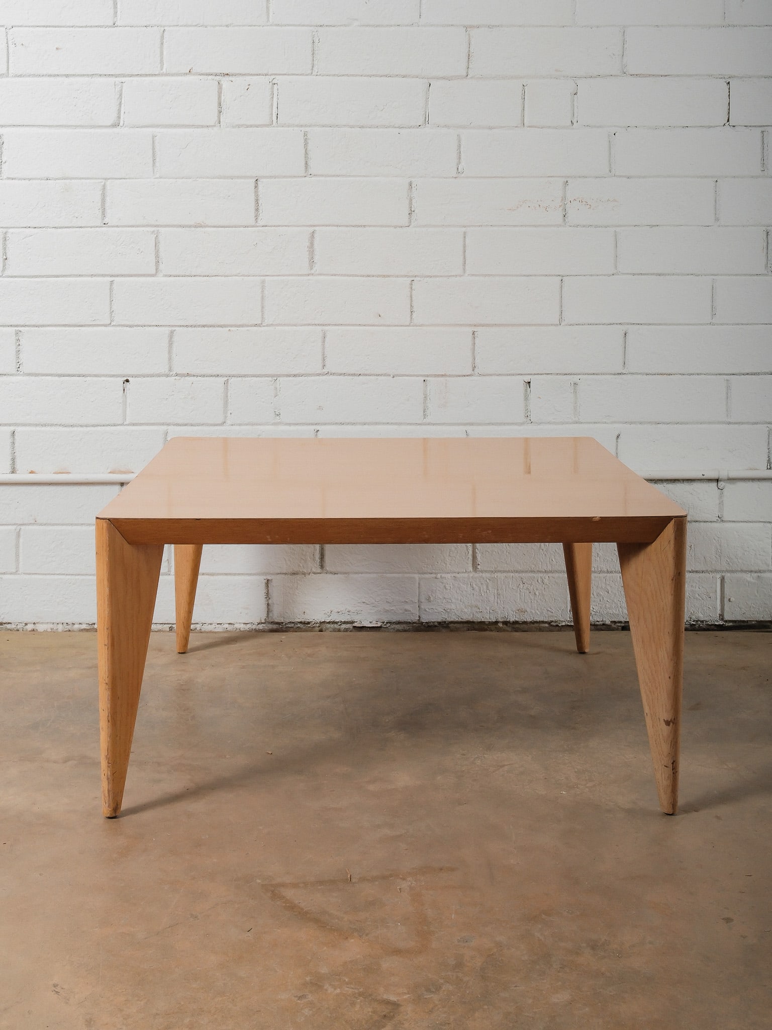 Square MCM Coffee Table: This mid-century modern coffee table features a square top with a clean, minimalist profile and four gently tapered legs. Finished in a light wood tone, the table simple construction and balanced prop