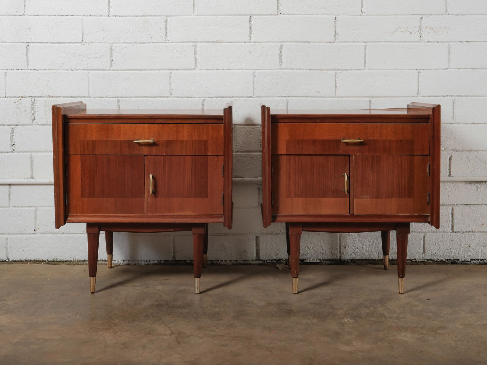 MCM Nightstands: This matching pair of mid-century modern cabinets each features a single drawer above double cabinet doors with minimalist metal hardware. Finished in a warm wood tone and raised on tapered legs with