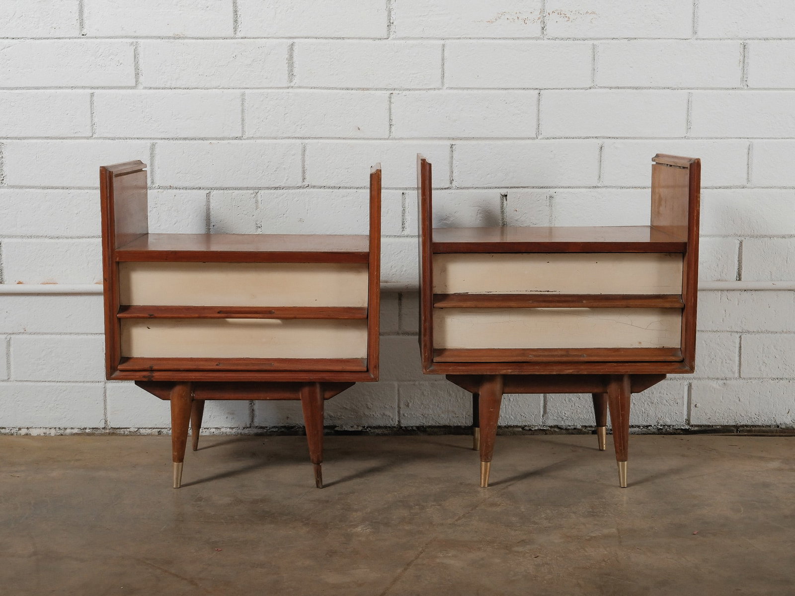 MCM Nightstands: This matching pair of mid-century modern nightstands features compact cases with open shelving and a single drawer each. Finished in a warm wood tone, the nightstands rest on tapered legs with brass-t