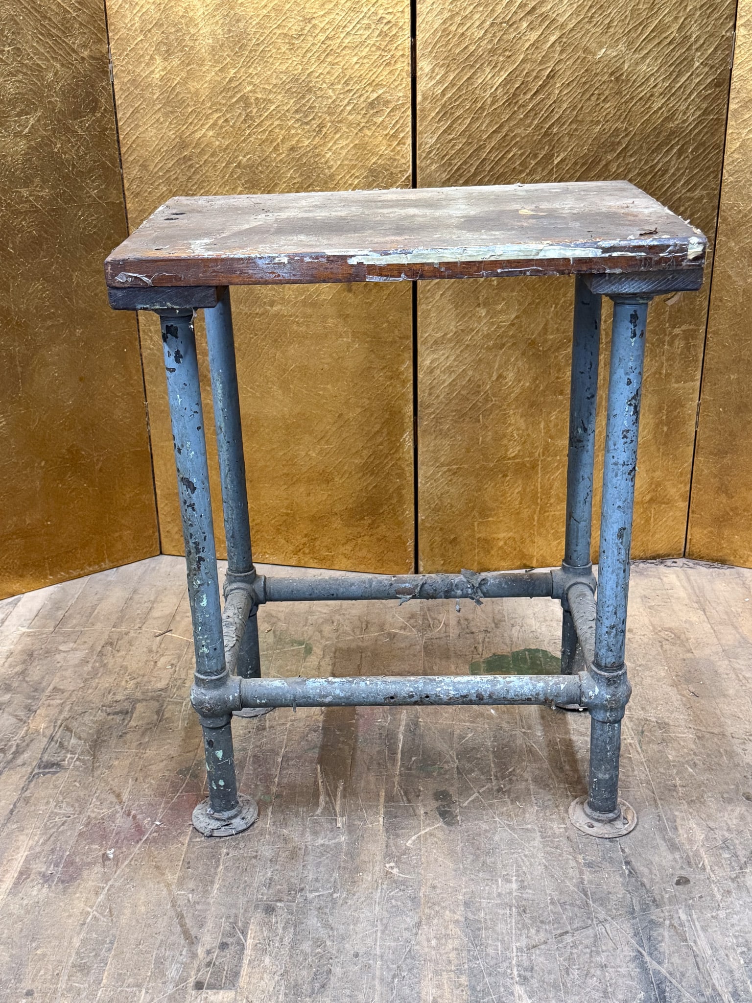 Industrial Metal Pipe Work Table with Wood Top: Industrial-style work table featuring a solid wood top with a distressed painted finish set on a sturdy metal pipe frame. The base is constructed from heavy steel piping with cross supports and
