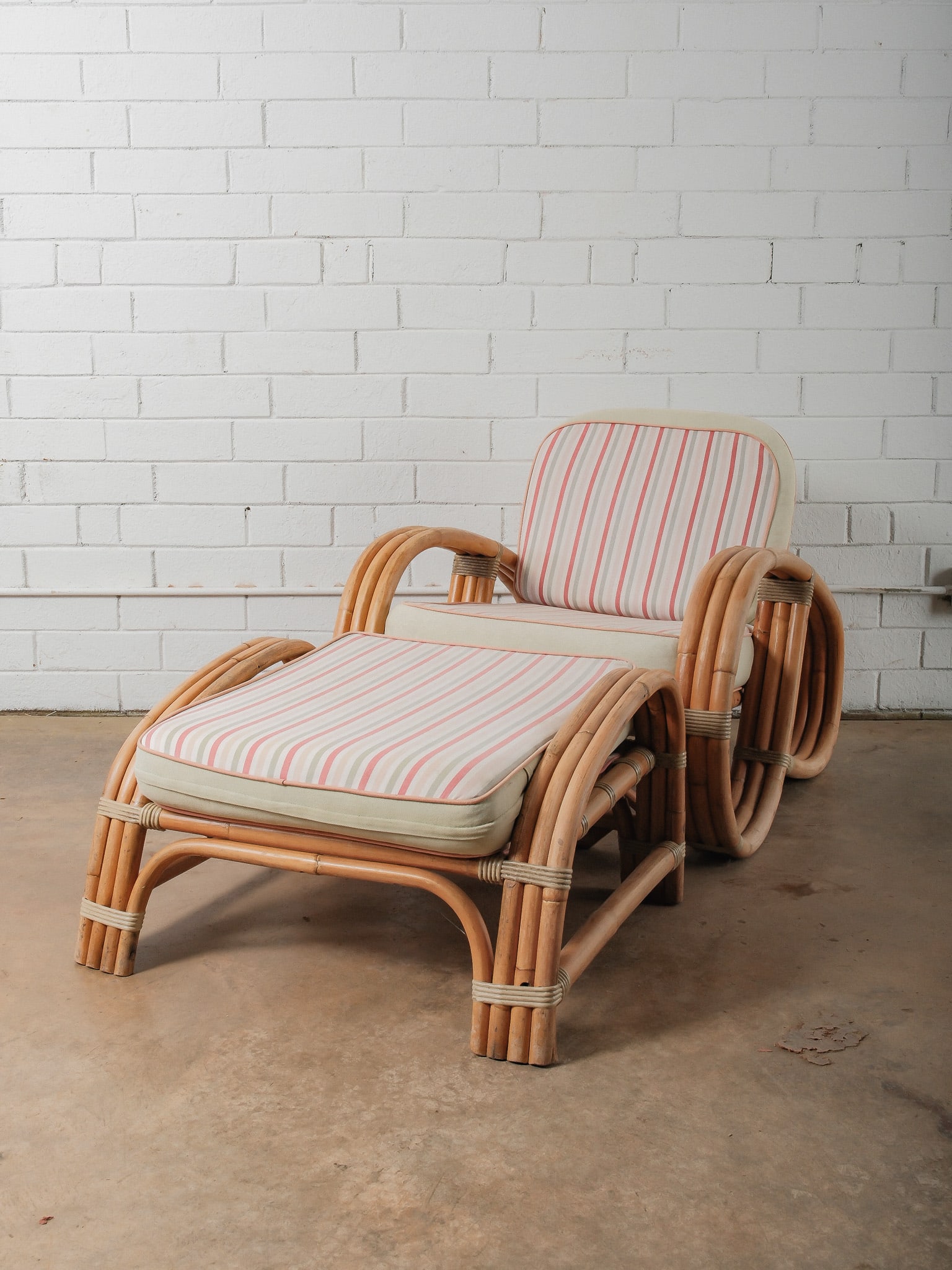 MCM Ratan Lounge Chair and Ottoman: This mid-century lounge chair features a sculptural rattan frame with rounded arms and layered curved supports. The chair is fitted with loose seat and back cushions upholstered in a striped fabric, a