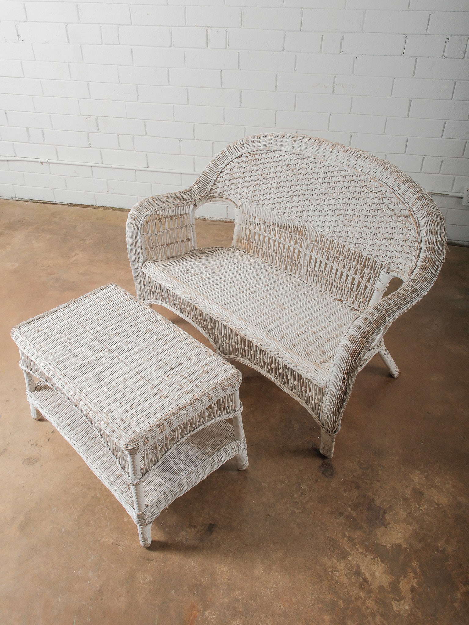 Painted Wicker Loveseat with Matching Table: White painted wicker loveseat with rolled arms and decorative openwork apron, accompanied by coordinating two-tier wicker side table. Cottage or porch style. Perfect for your porch or sunroom this Spr