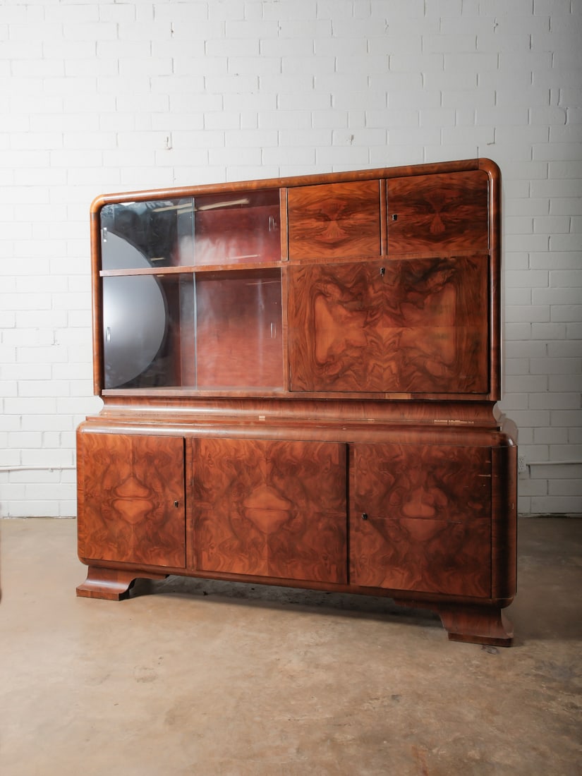 Art Deco Style Burl Wood Sideboard: Two-piece sideboard with rounded corners and dramatic book matched burl veneer. Upper cabinet with sliding glass doors and wood panel doors; lower cabinet with concealed storage.