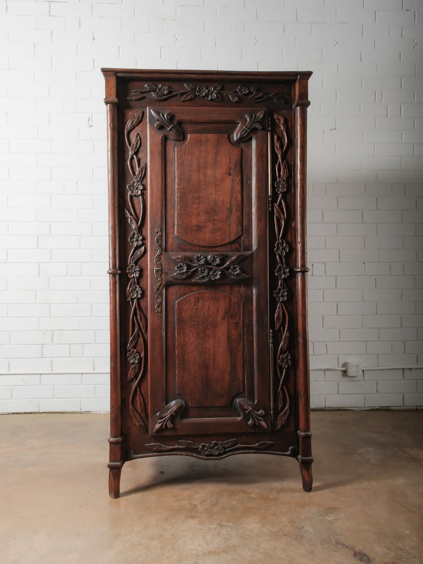 Carved Wood Armoire: Tall single-door armoire featuring extensive carved floral and vine motifs, paneled door, and shaped base. Traditional European styling.