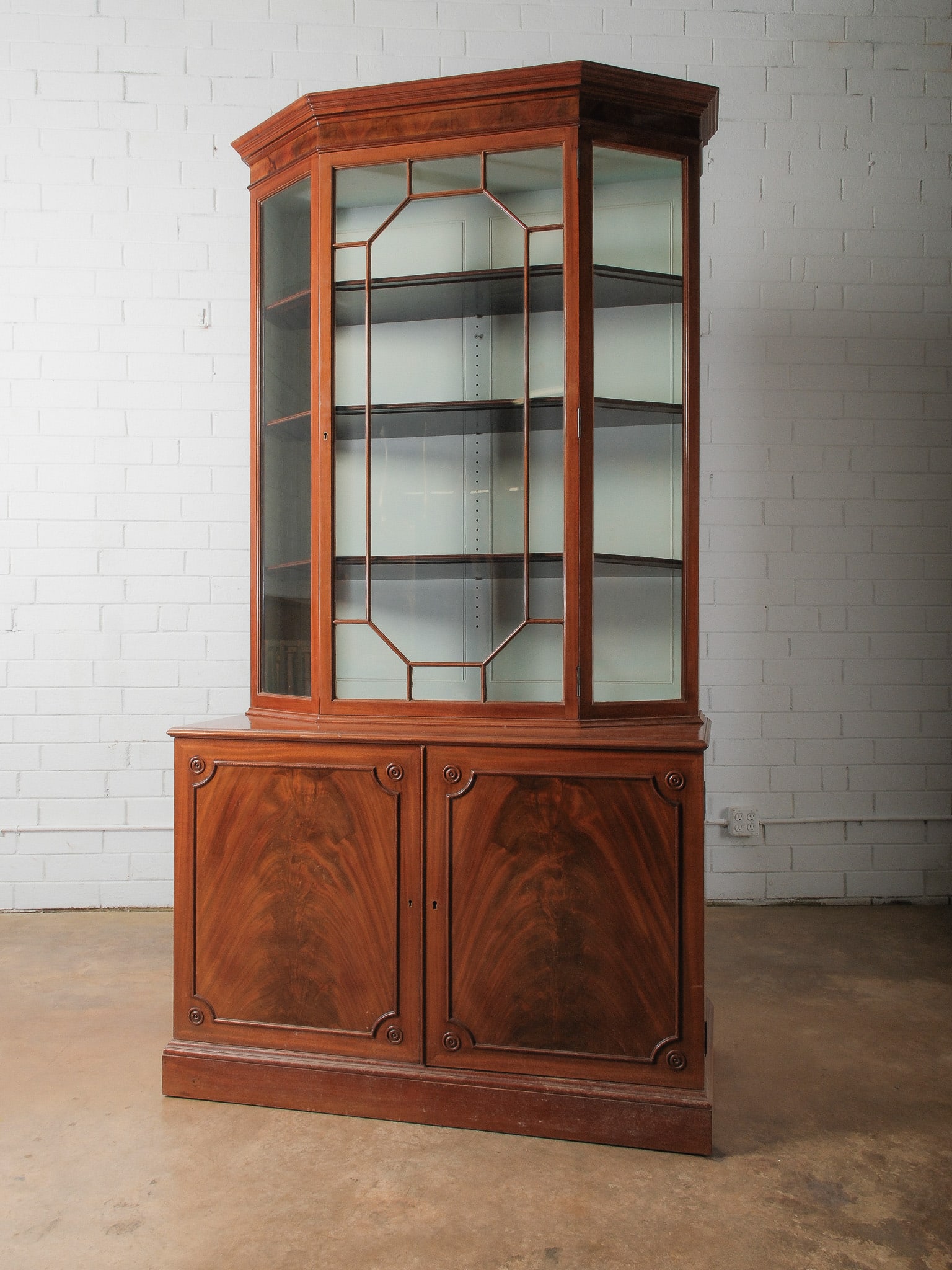Mahogany Two-Part Glazed Corner Cabinet: Elegant two-part China cabinet crafted in richly grained mahogany. The upper section features glass doors with geometric muntin detailing and interior shelving. The lower cabinet includes paneled