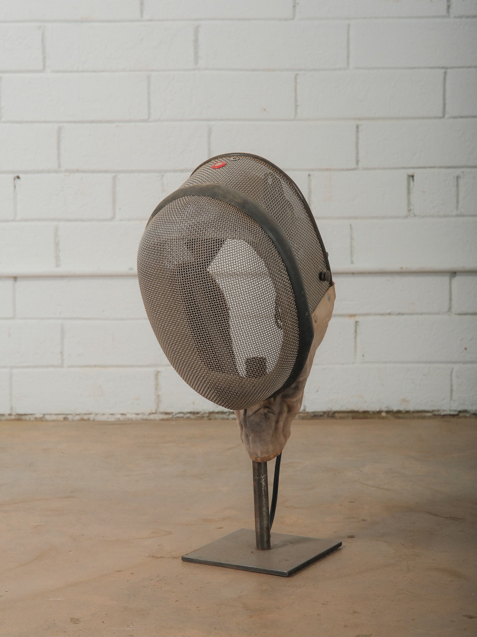 Vintage Fencing Mask Lamp: Decorative lamp constructed from a vintage fencing mask mounted on a metal stand base. The mask features a traditional metal mesh face guard with interior padding and retains the aged patina and wear