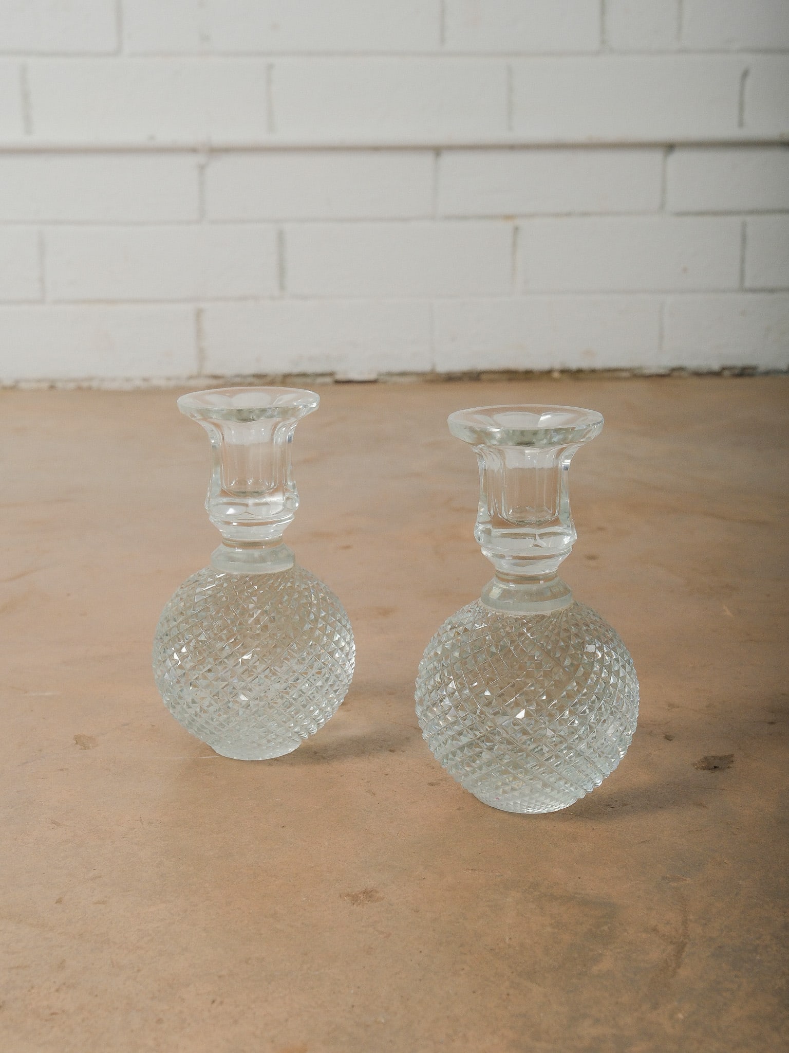Pair of Crystal Candlesticks: Pair of crystal candlesticks featuring diamond-patterned globular bases with flared candle holders and faceted detailing that reflects light beautifully. The clear crystal construction is in like-new