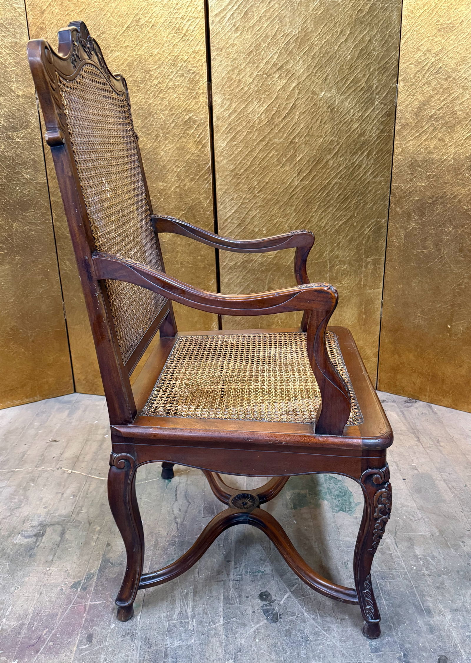Caned Armchair with Carved Wood Frame: Beautiful armchair crafted from carved wood with cane back and seat. The frame features decorative carvings along the crest rail, arms, and apron, along with cabriole legs joined by an X-form