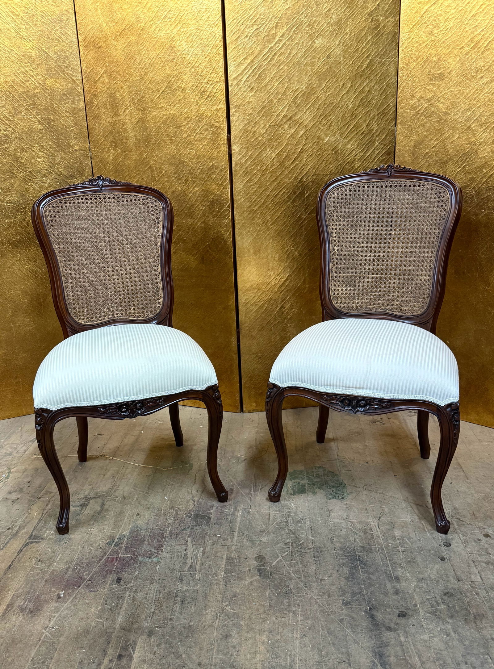 Pair of Louis XV Style Cane Back Armless Chairs w/ Cream Stripe Cushions: Elegant pair of Louis XV style side chairs featuring carved wooden frames with cane backs and upholstered seats. The chairs display graceful cabriole legs and floral carved detailing along the apron a