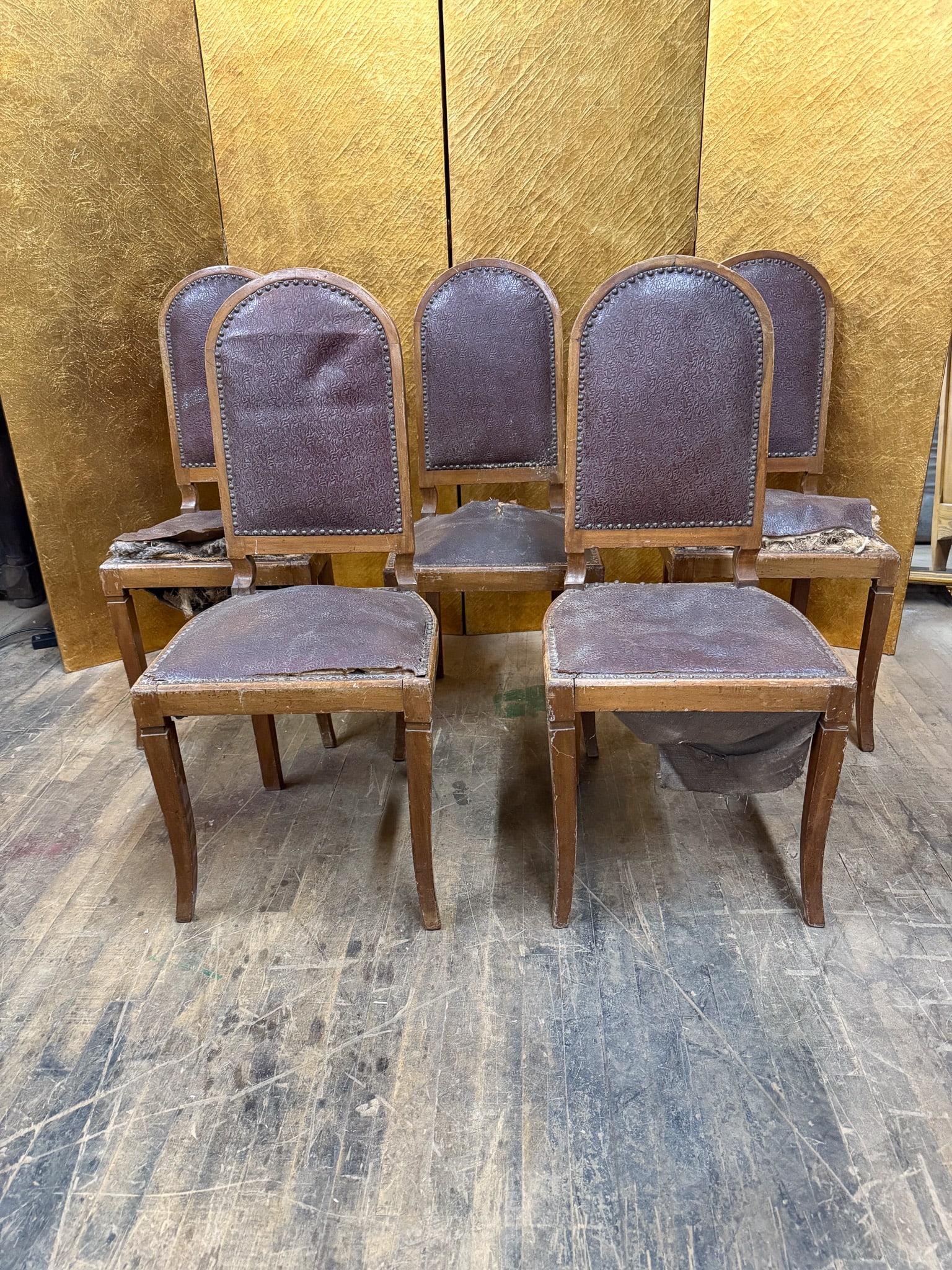 Set of 5 Distressed Leather Dining Chairs for Restoration: Set of five dining chairs featuring wooden frames with arched backs upholstered in maroon leather with decorative nail head trim. The chairs show heavy wear and distressing to the leather upholstery,