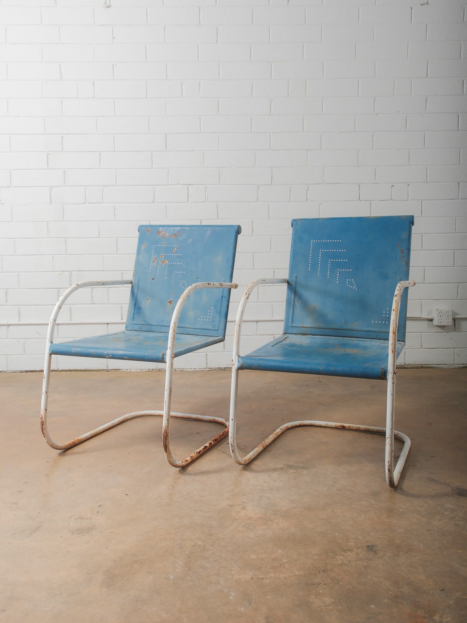 Pair of Vintage Blue Metal Lawn Chairs: Two mid-century style metal lawn chairs with perforated back design and white tubular metal frames. Finished in worn blue paint with natural patina. Classic cantilever form makes them ideal for your