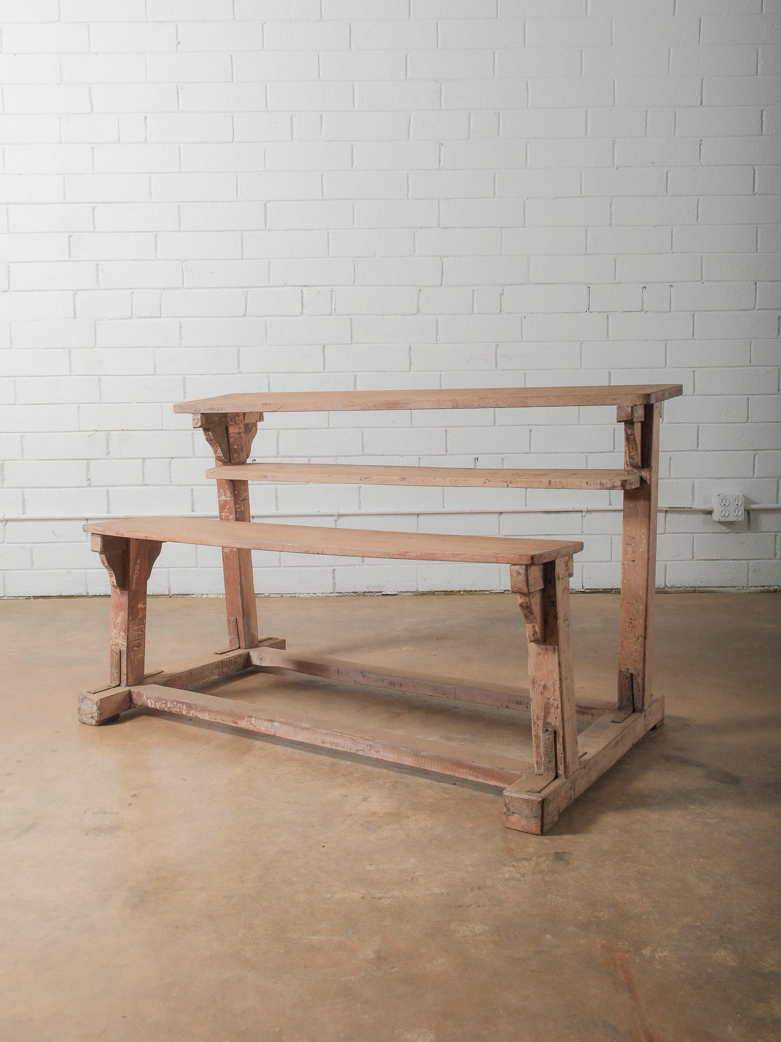 Double Wooden School Desk: Solid wood double school desk featuring a lower bench seat and upper shelf with thick plank construction and mortise-style joinery. The worn surface and visible age marks give it authentic workshop ch