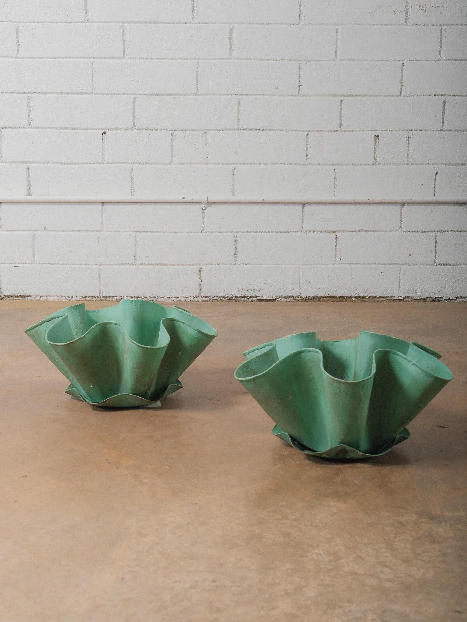 Pair of Sculptural Green Glazed Planters: Pair of decorative planters featuring a dramatic fluted, petal-form silhouette with softly scalloped edges. Finished in a matte green glaze with subtle surface variation. Their organic shape makes the