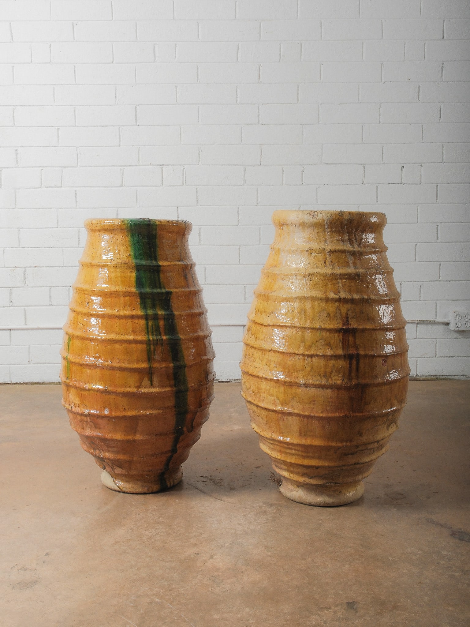 Pair of Large Glazed "Beehive" Ceramic Vessels: Pair of substantial ceramic vessels featuring horizontal ribbing and warm amber glaze with natural drips in green and brown tones. The glossy surface and organic glaze movement give each piece strong