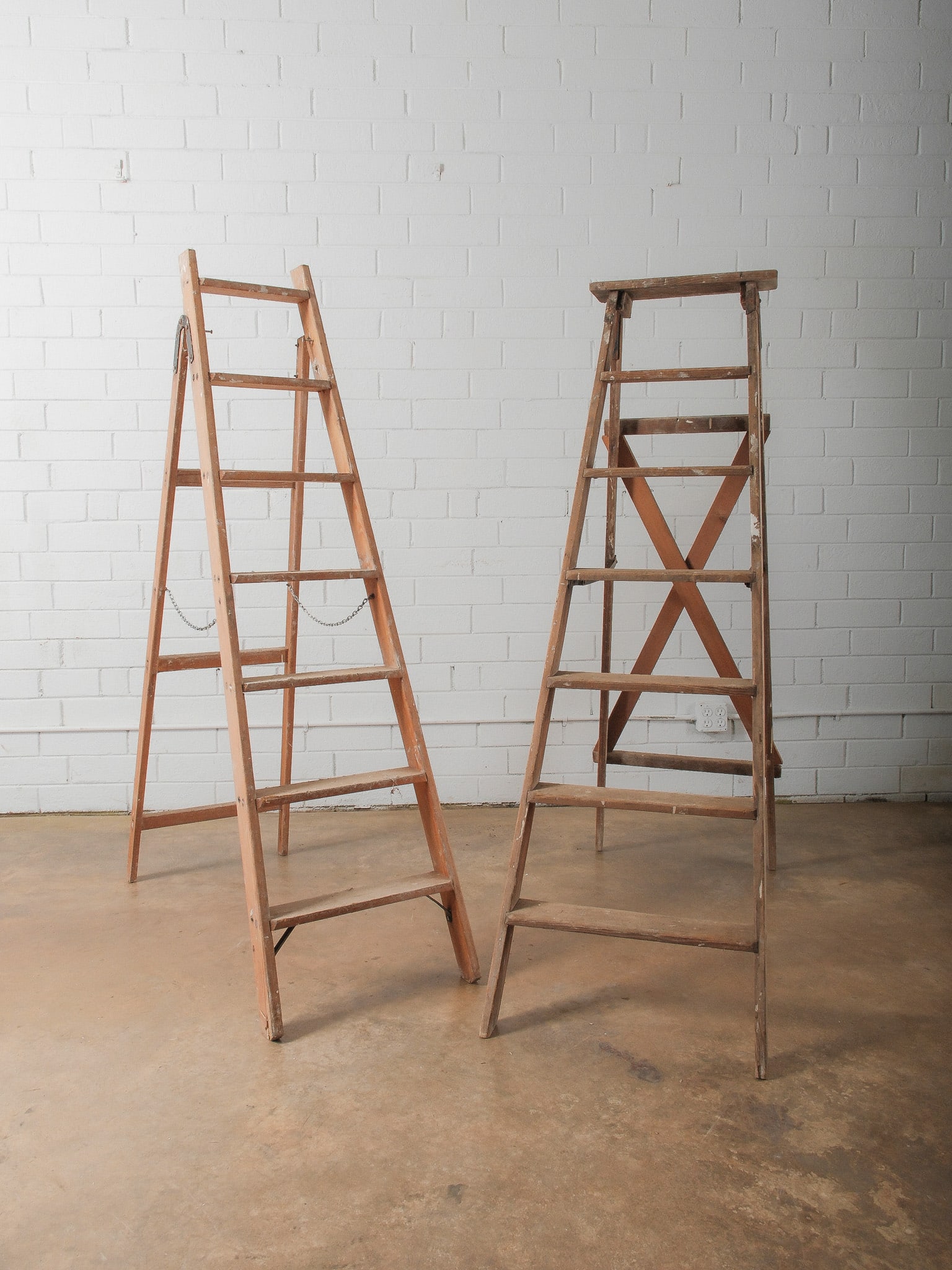 Pair of Vintage Wooden Step Ladders: Pair of wooden step ladders featuring classic A-frame construction with metal hinges and chain supports. The naturally worn surfaces and paint remnants add authentic character, making them ideal for