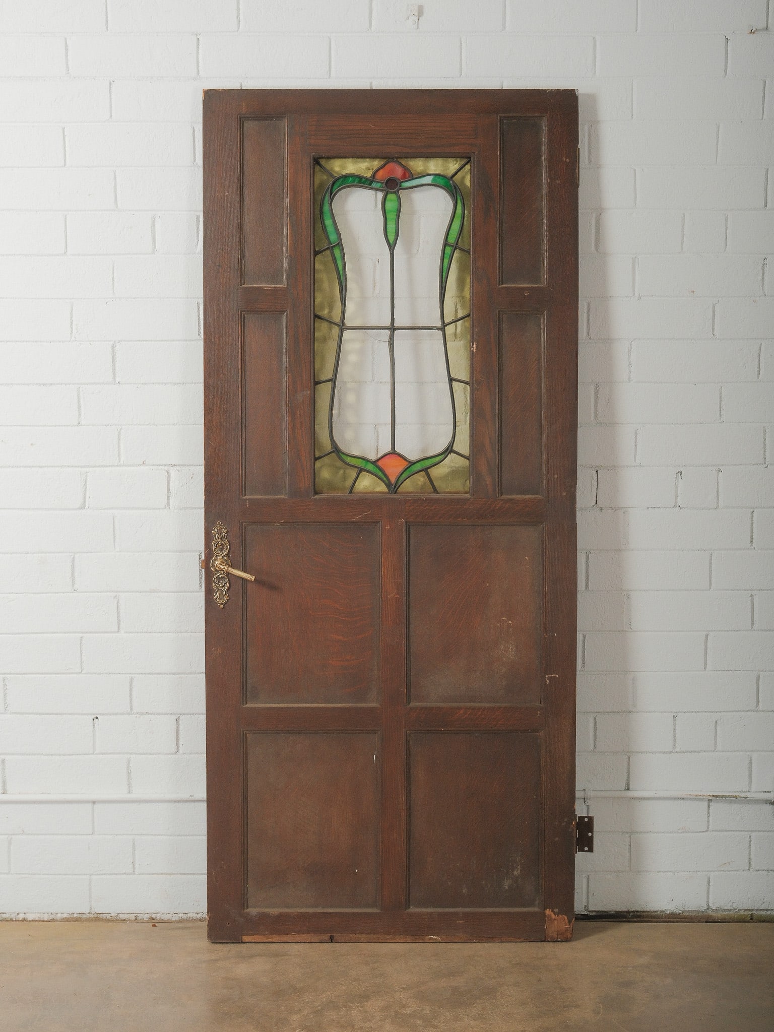 Stained Glass Wood Door: Antique wooden interior door featuring a central stained glass panel with green and amber accents in a decorative leaded design. The door includes paneled wood construction and retains original hardwa