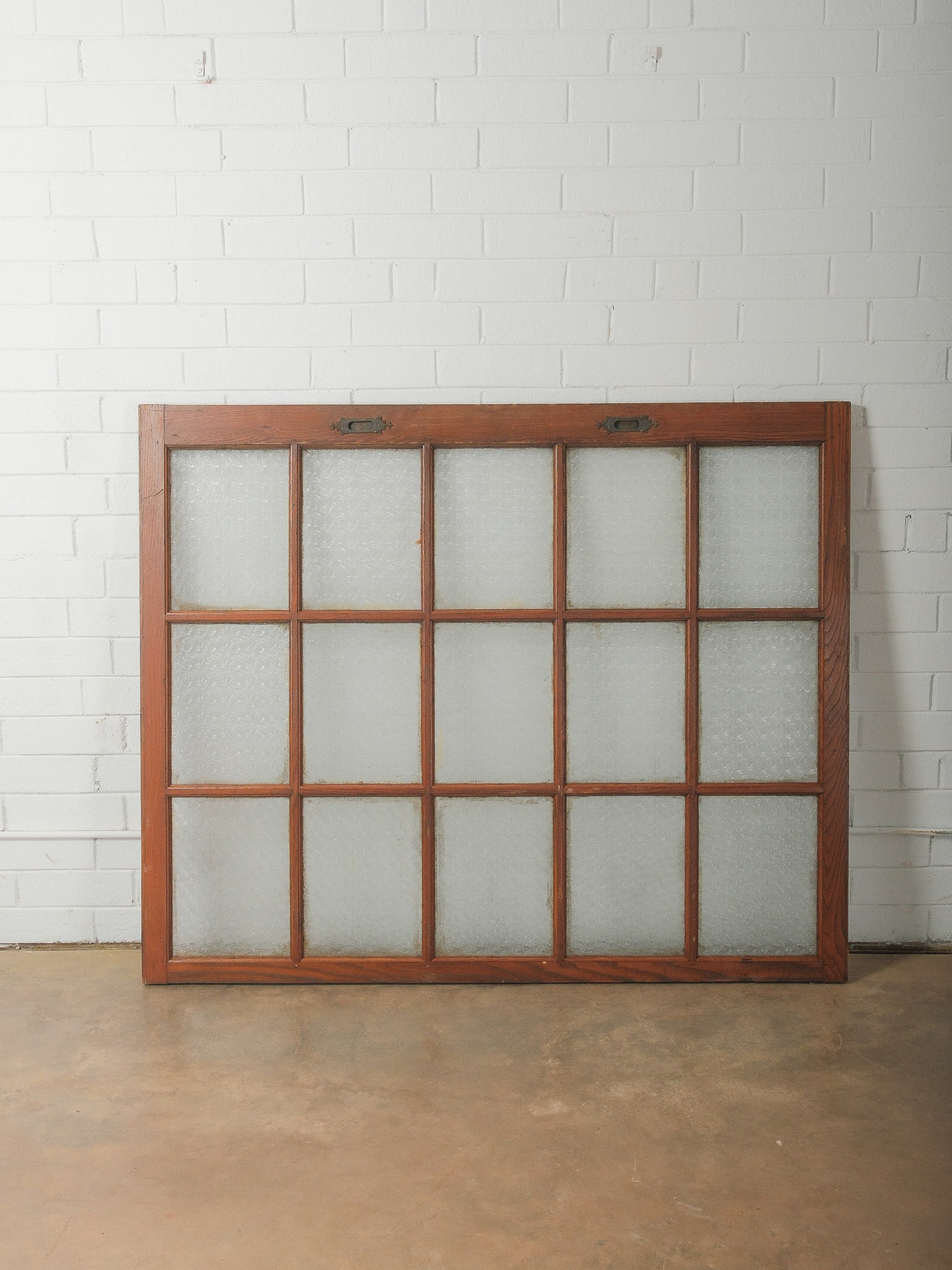 Large Multi-Pane Wood Window Frame: Large vintage wooden window frame featuring multiple rectangular clear glass panes within a solid wood muntin grid. The frame retains original metal hardware along the top and shows natural wear consi
