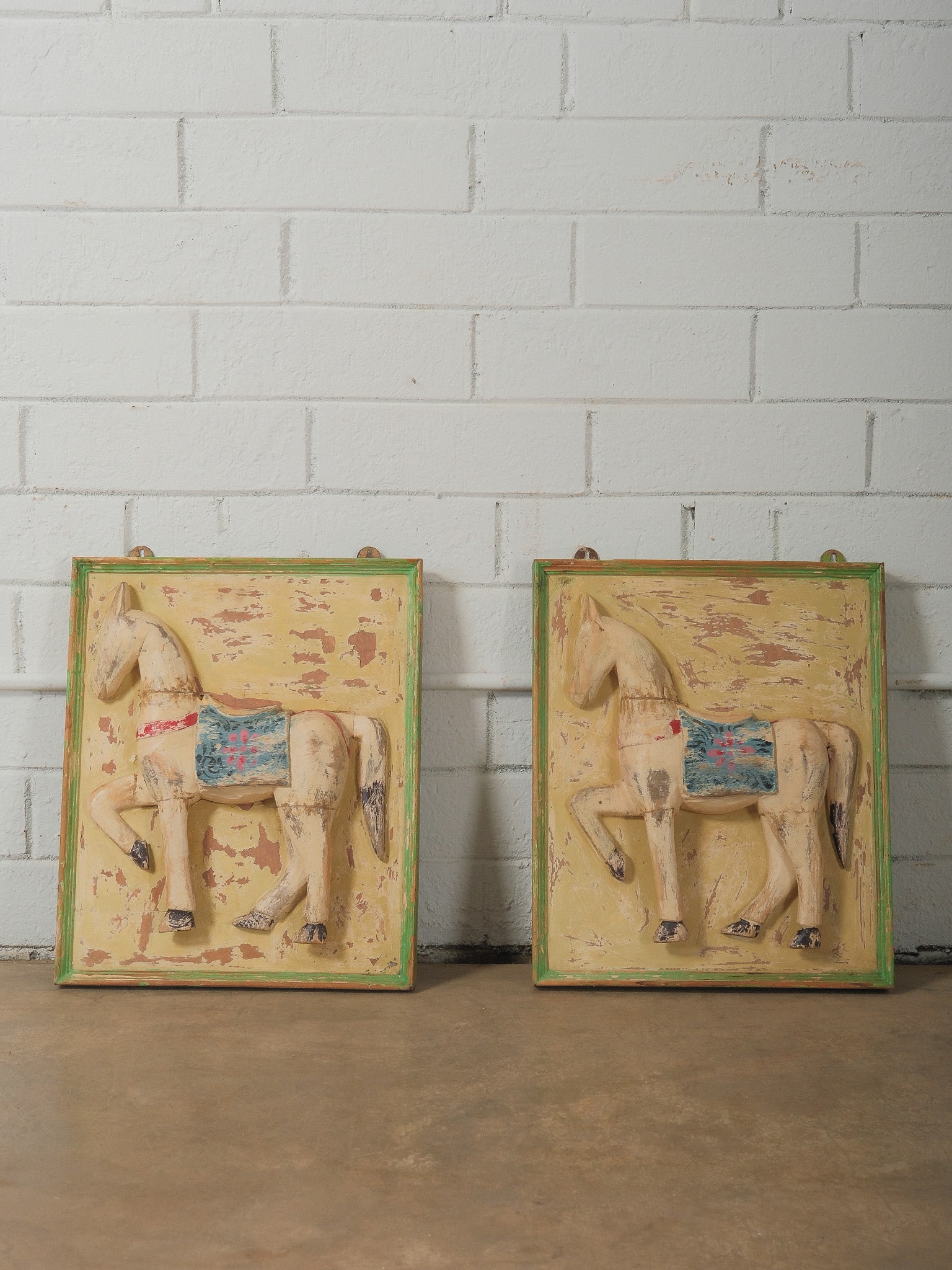 Pair of Painted Wooden Horse Wall Art: Pair of decorative carved wooden wall panels featuring raised carousel horse figures within painted frames. The panels retain distressed painted finishes in cream, yellow, green, and blue tones with v