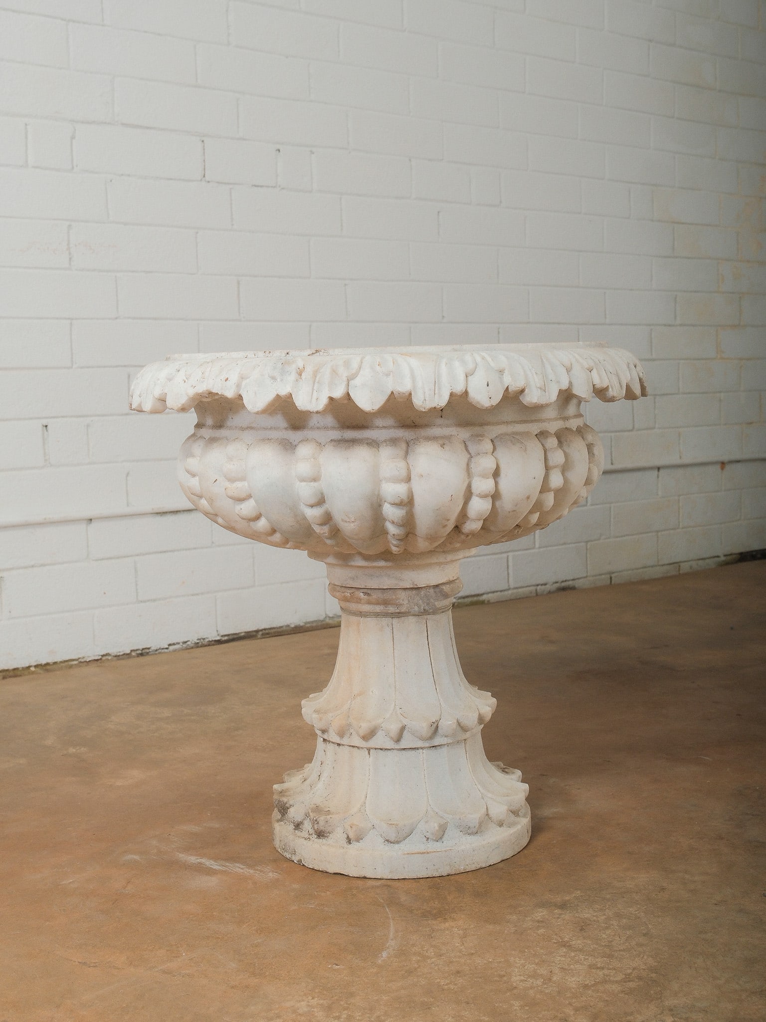 Carved Marble Garden Planter or Bird Bath: Decorative carved marble garden planter or bird bath featuring a wide scalloped rim with classical relief detailing and mounted on a pedestal base. The piece displays natural stone coloration and