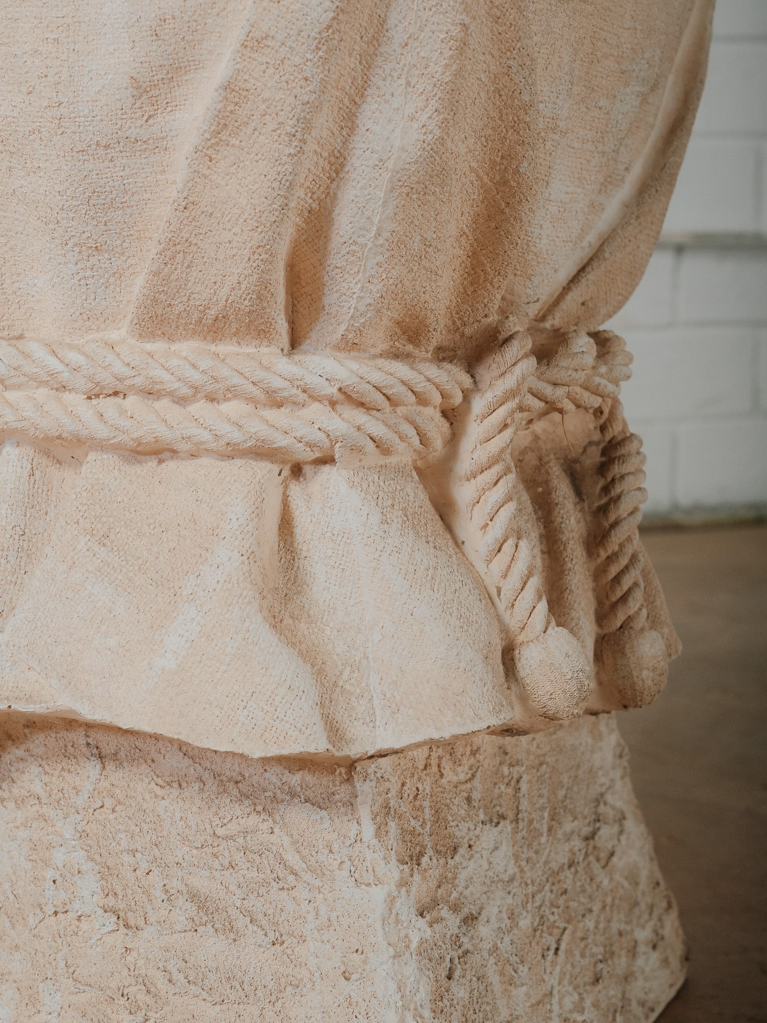 Plaster Garden Pedestal with Draped Fabric Motif: Decorative plaster garden pedestal featuring a sculptural trompe draped fabric design, accented with a rope-tied detail around the center. The textured base and hand-formed appearance give it a