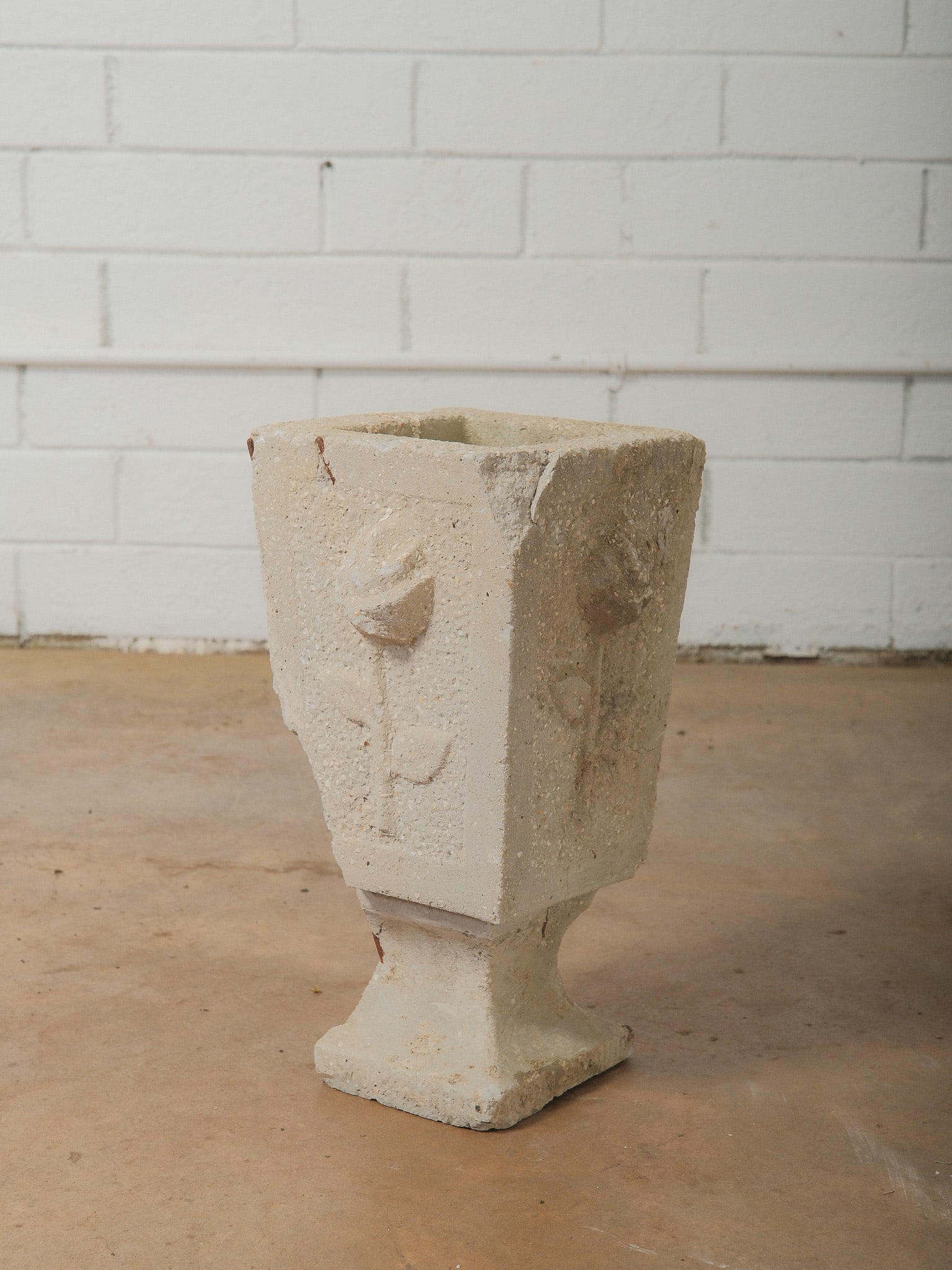 Concrete Pedestal Planter with Relief Decoration: Concrete pedestal planter featuring a square tapered body with raised floral relief decoration on each side and a stepped pedestal base. The piece shows natural weathering and patina consistent with o