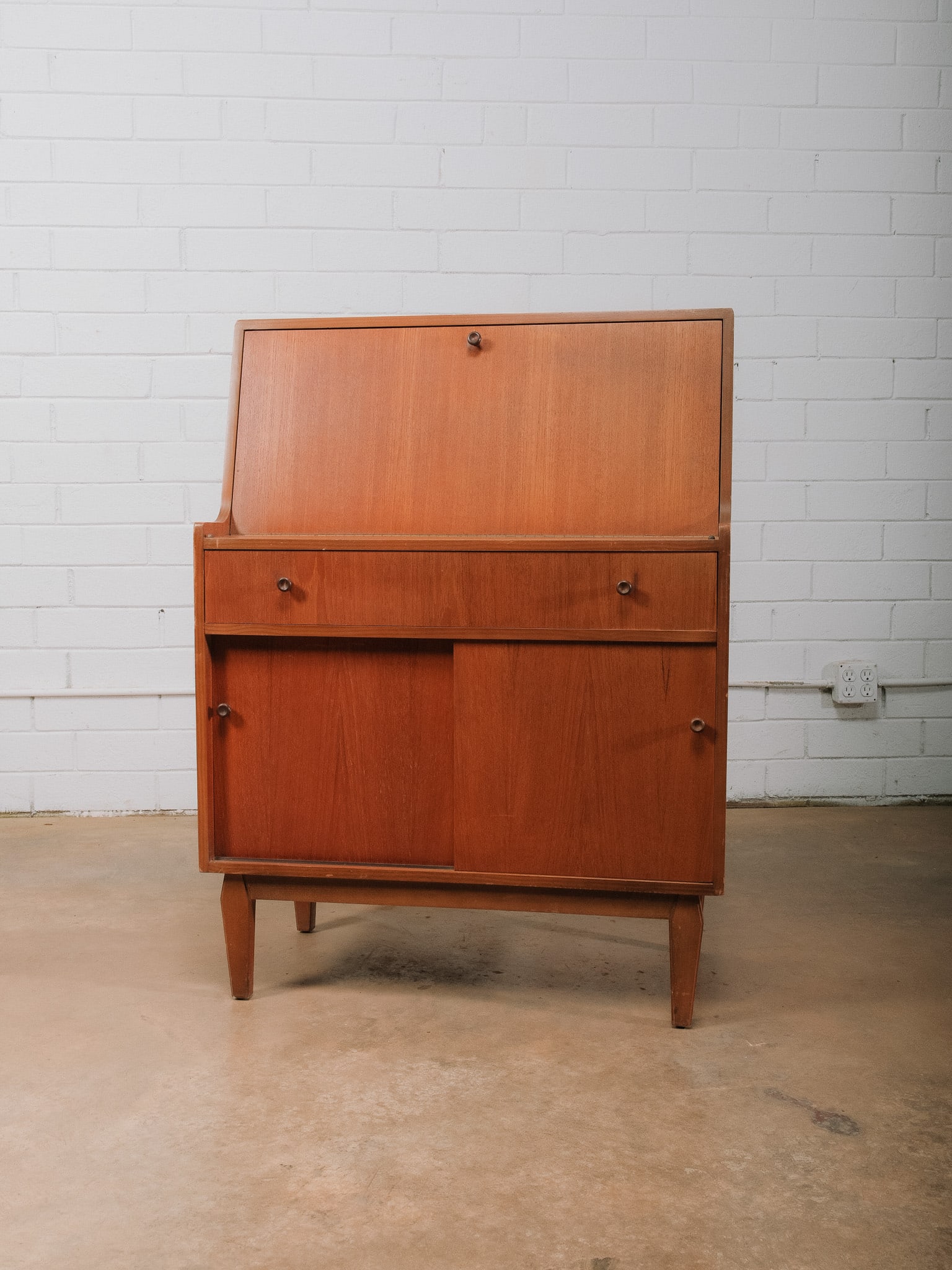 MCM Secretary Cabinet: Mid-century modern secretary cabinet featuring a fall-front writing surface, a full-width drawer, and a lower storage compartment with sliding cabinet doors. Raised on tapered legs, this versatile