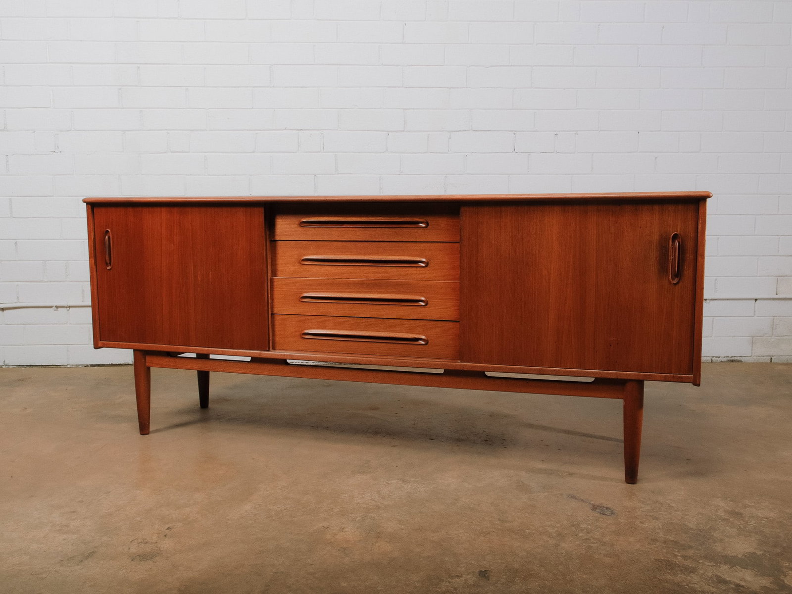 MCM Credenza: Mid-century modern credenza featuring two sliding cabinet doors flanking a bank of four center drawers with integrated sculpted pulls. Raised on tapered legs, this well-proportioned sideboard offers