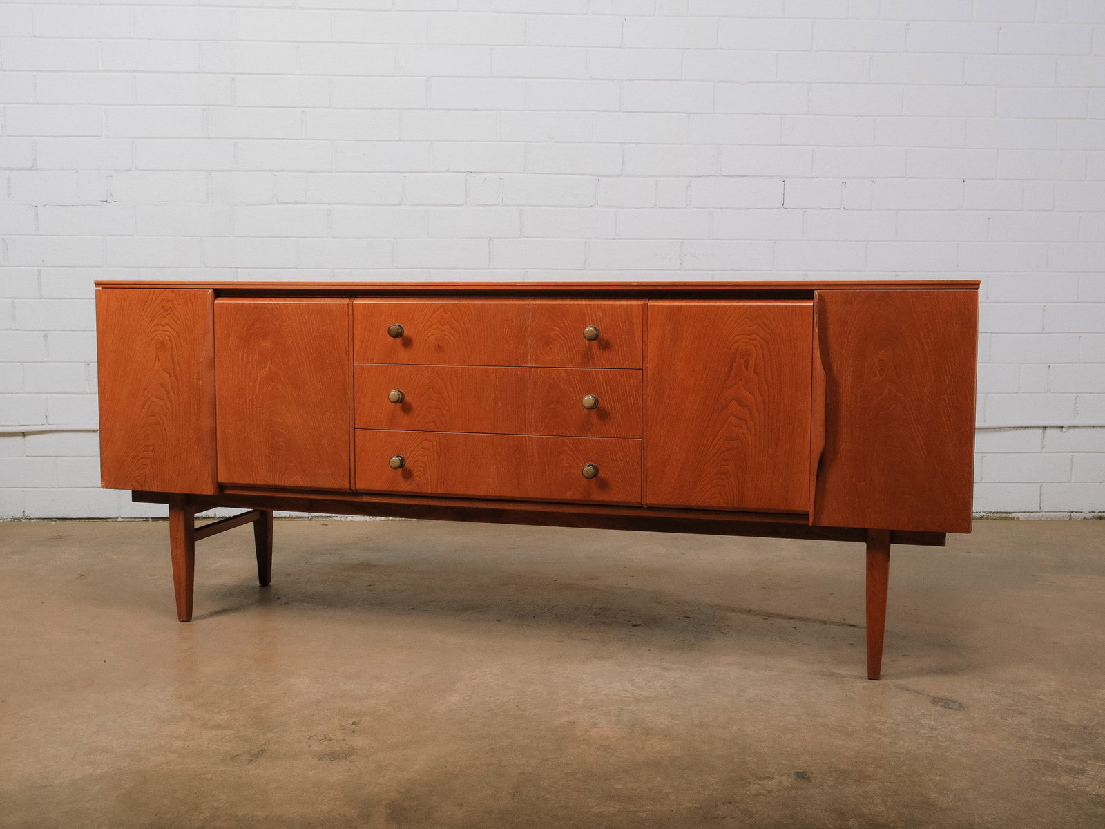MCM Sideboard: Mid-century modern sideboard featuring three center drawers flanked by two spacious storage compartments behind cabinet doors. Raised on tapered legs with simple round wooden pulls, the cabinet