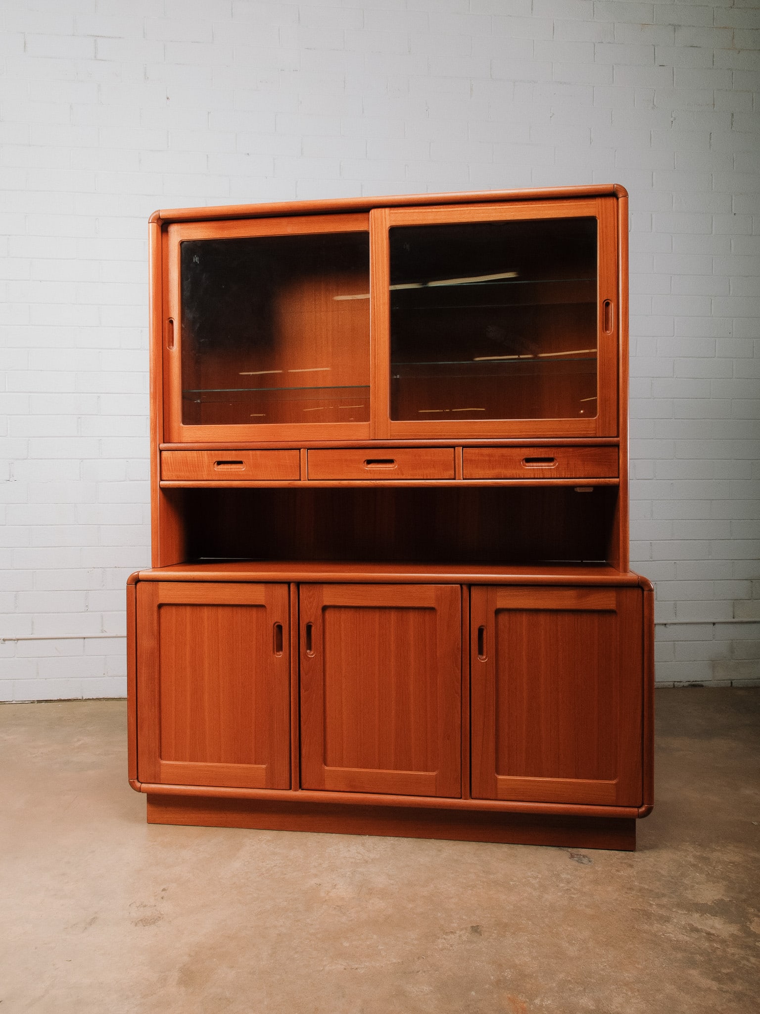 MCM Credenza with Sliding Glass Doors: Two-piece mid-century modern display hutch featuring an upper cabinet with sliding glass doors enclosing glass display shelves over three shallow accessory drawers and an open serving shelf. The lower