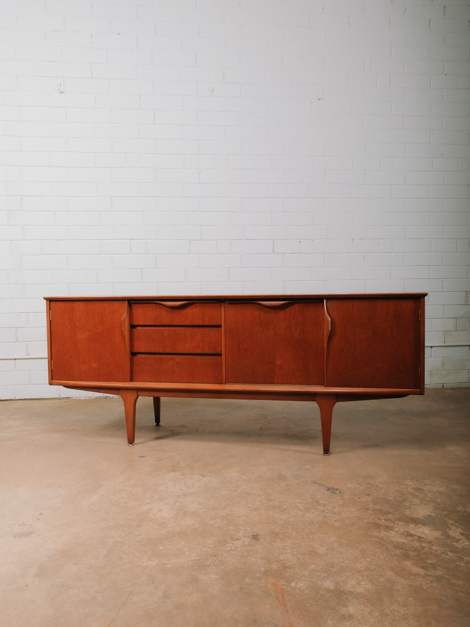MCM Sideboard: Mid-century modern sideboard featuring three center drawers flanked by cabinet doors opening to spacious interior storage compartments. Raised on sculptural tapered legs with brass-capped feet, clean