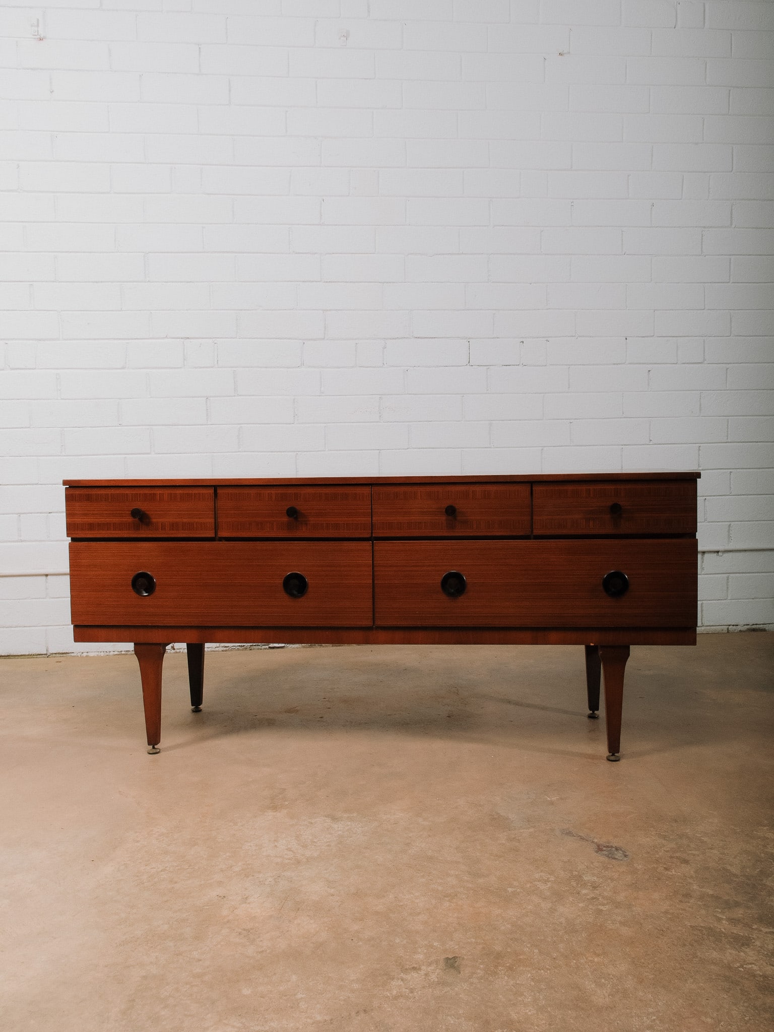 MCM Sideboard: Mid-century modern sideboard with beautifully inlaid drawer fronts with striking circular pulls and raised on tapered legs. This handsome case piece showcases clean architectural lines, warm wood