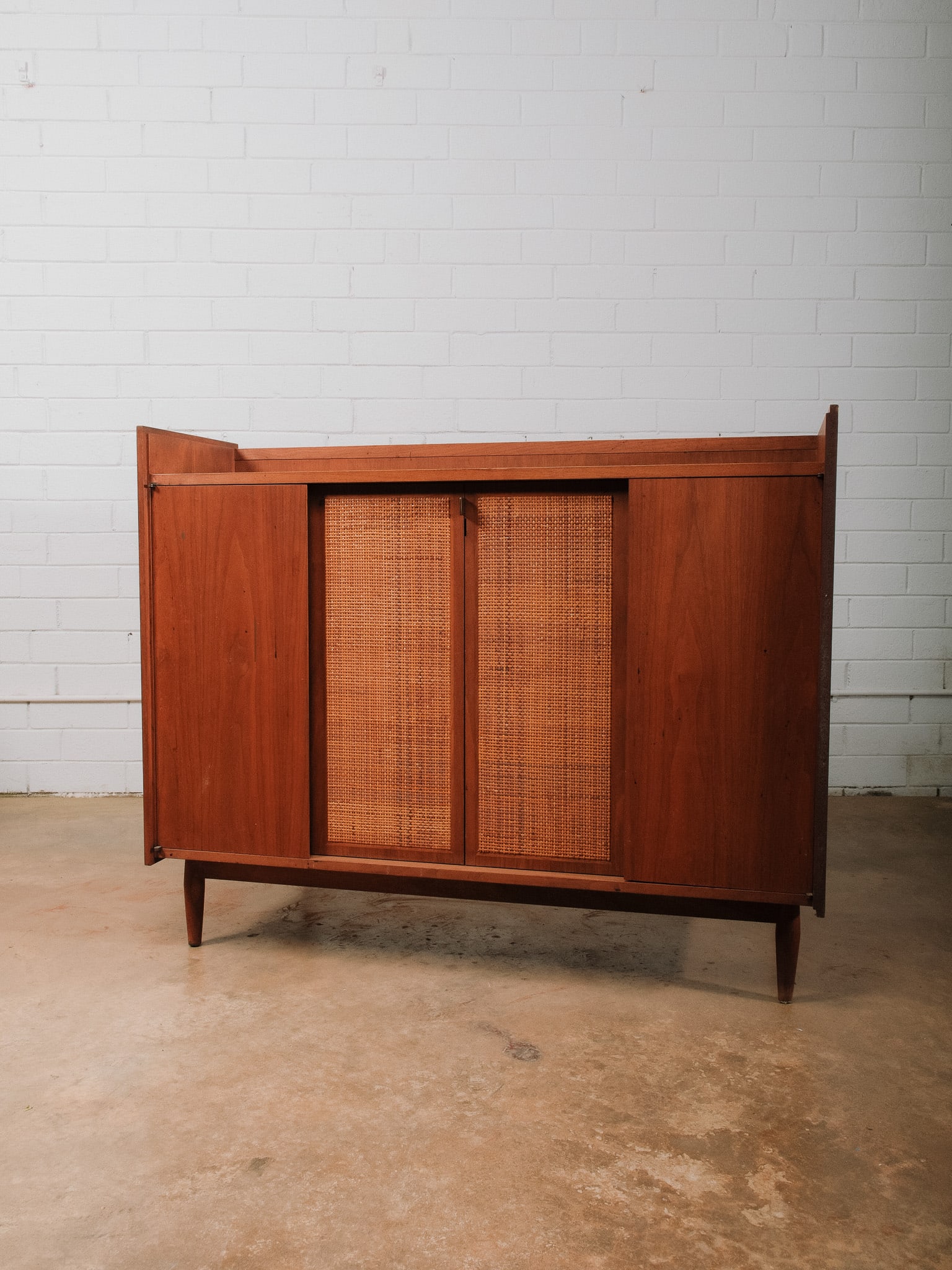 Mid-Century Record Cabinet / Bar Cabinet: Mid-century modern cabinet featuring woven cane sliding doors, tapered legs, and a versatile interior. The top includes a black laminate work surface with cutouts designed for record player