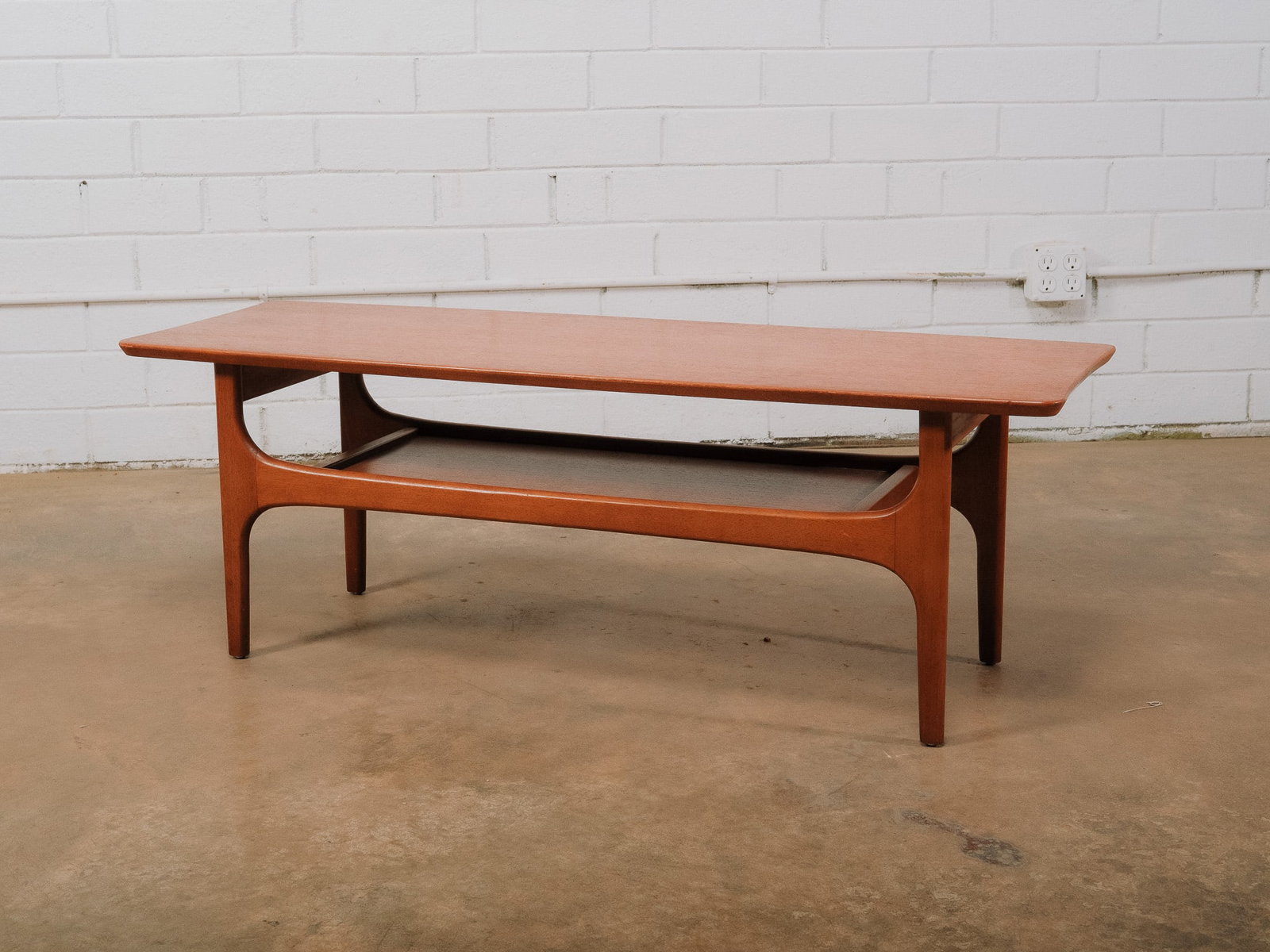 MCM Small Coffee Table: Mid-century modern coffee table featuring a spacious rectangular top above a lower open display shelf. Gracefully sculpted supports and rounded edges create the clean organic lines characteristic of