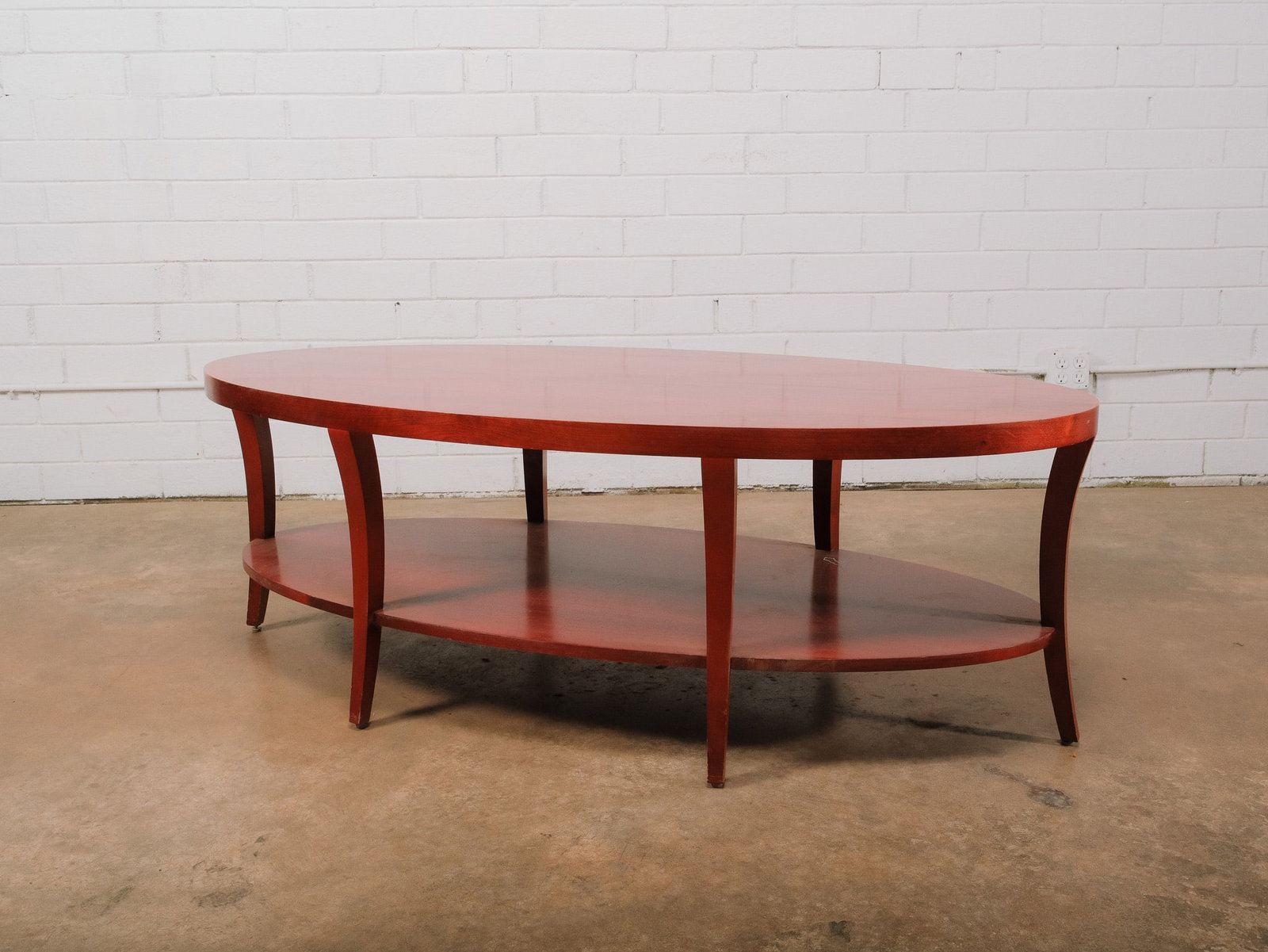 Contemporary Oval Coffee Table: Contemporary oval wood coffee table featuring a rich reddish-brown finish, gracefully curved legs, and a matching lower display shelf for additional storage or décor. The clean, elegant silhouette ma