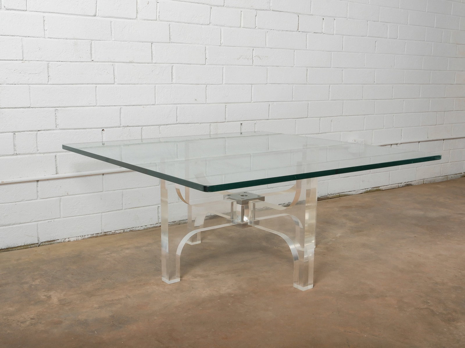 MCM Glass and Lucite Coffee Table: A sleek modern coffee table featuring a clear glass top supported by a sculptural lucite base with curved legs and central mounting hardware. The transparent base creates a light, architectural look