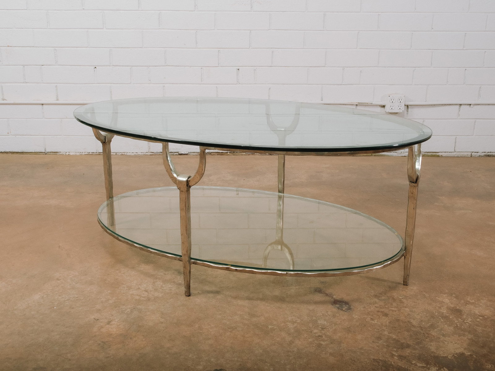 Oval Glass and Metal MCM Coffee Table: Mid-century modern oval coffee table featuring a clear glass top and matching lower glass shelf supported by a sculptural polished metal frame. The two-tier design provides additional display or stora