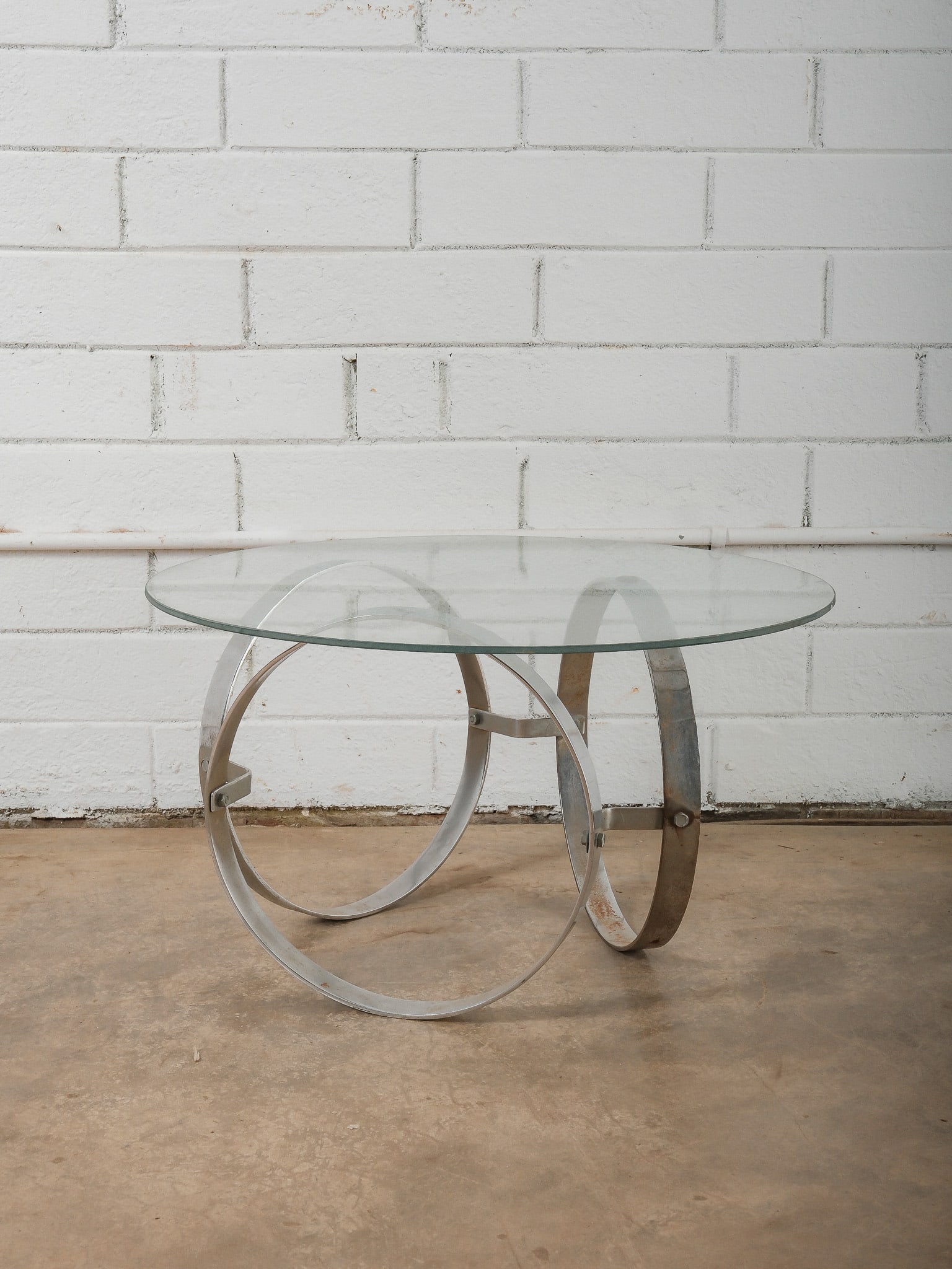 Modern Glass-Top Cocktail Table with Sculptural Metal Base: This modern table features a circular glass top supported by a sculptural metal base composed of curved ring forms. The open, architectural base creates a striking visual contrast with the