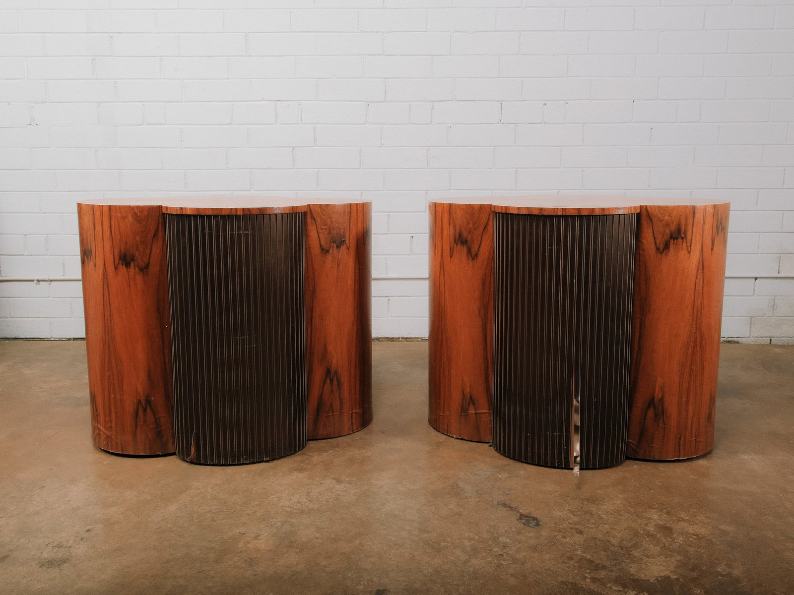 Pair of MCM Clover-Shaped Accent Tables: Pair of mid-century modern clover-shaped accent tables featuring warm wood veneer bodies with contrasting ribbed dark metal center panels. Their sculptural three-lobed form creates a distinctive profi