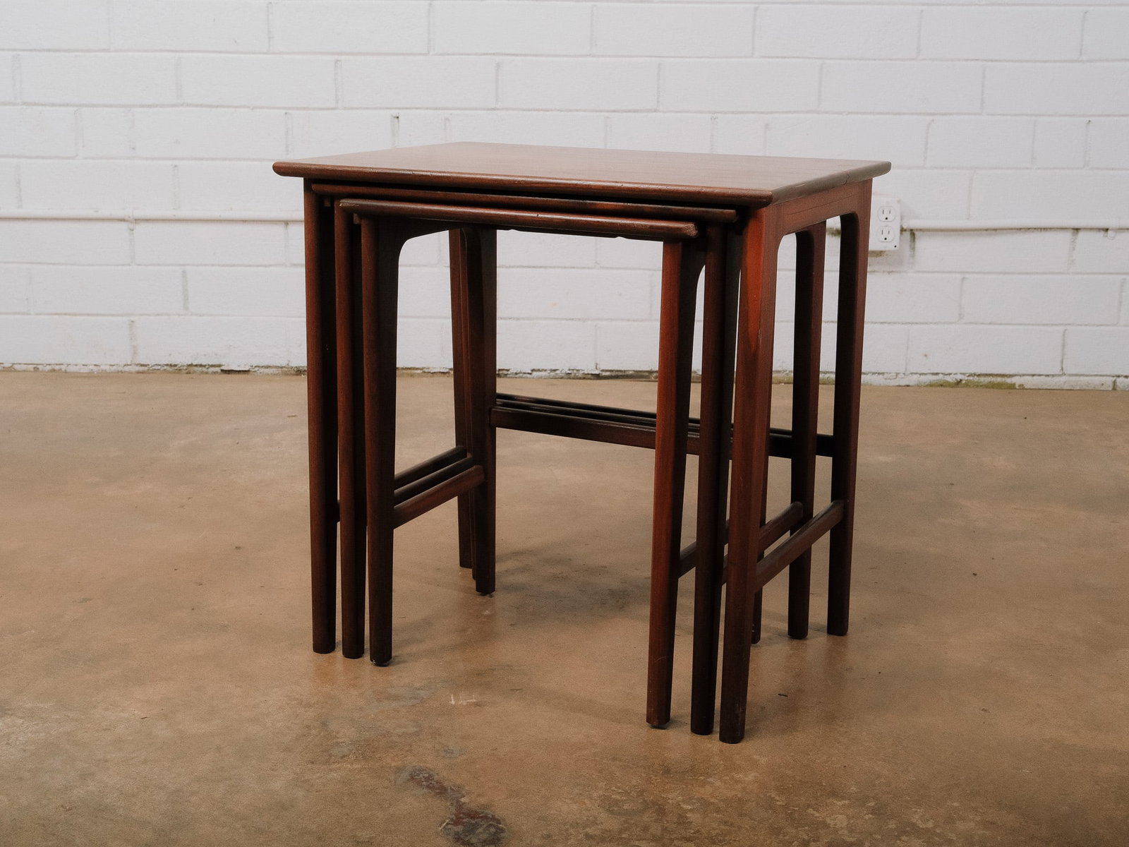 Set of Three Nesting Tables: Set of three mid-century modern nesting tables with rectangular tops, tapered legs, and warm wood grain. The graduated sizes allow the tables to nest together for compact storage or separate for flexi