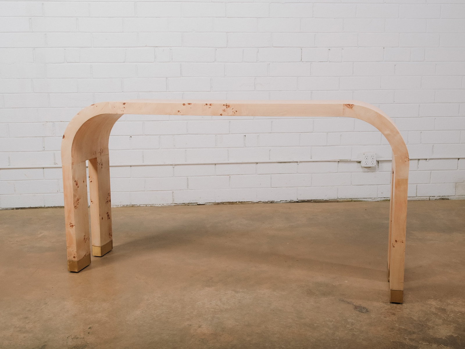 Modern Burl Wood Veneer Console Table: Modern console table featuring a striking waterfall silhouette crafted with burl wood veneer over a rectangular frame. The clean, sculptural form is accented by rounded corners and brass-capped feet, 